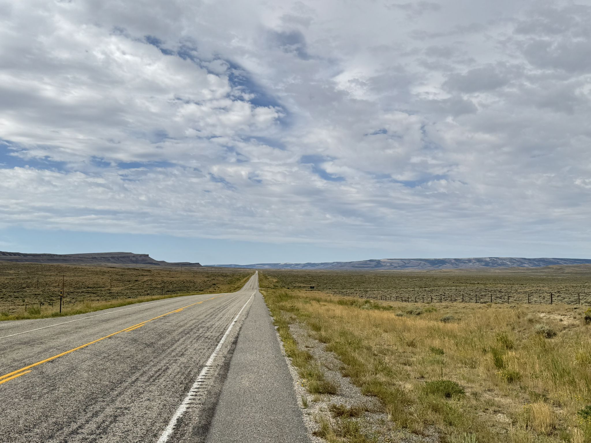 A paved road extends through a flat, dry landscape under an overcast sky. - Sage Creek Road (Rawlins to Sage Creek)