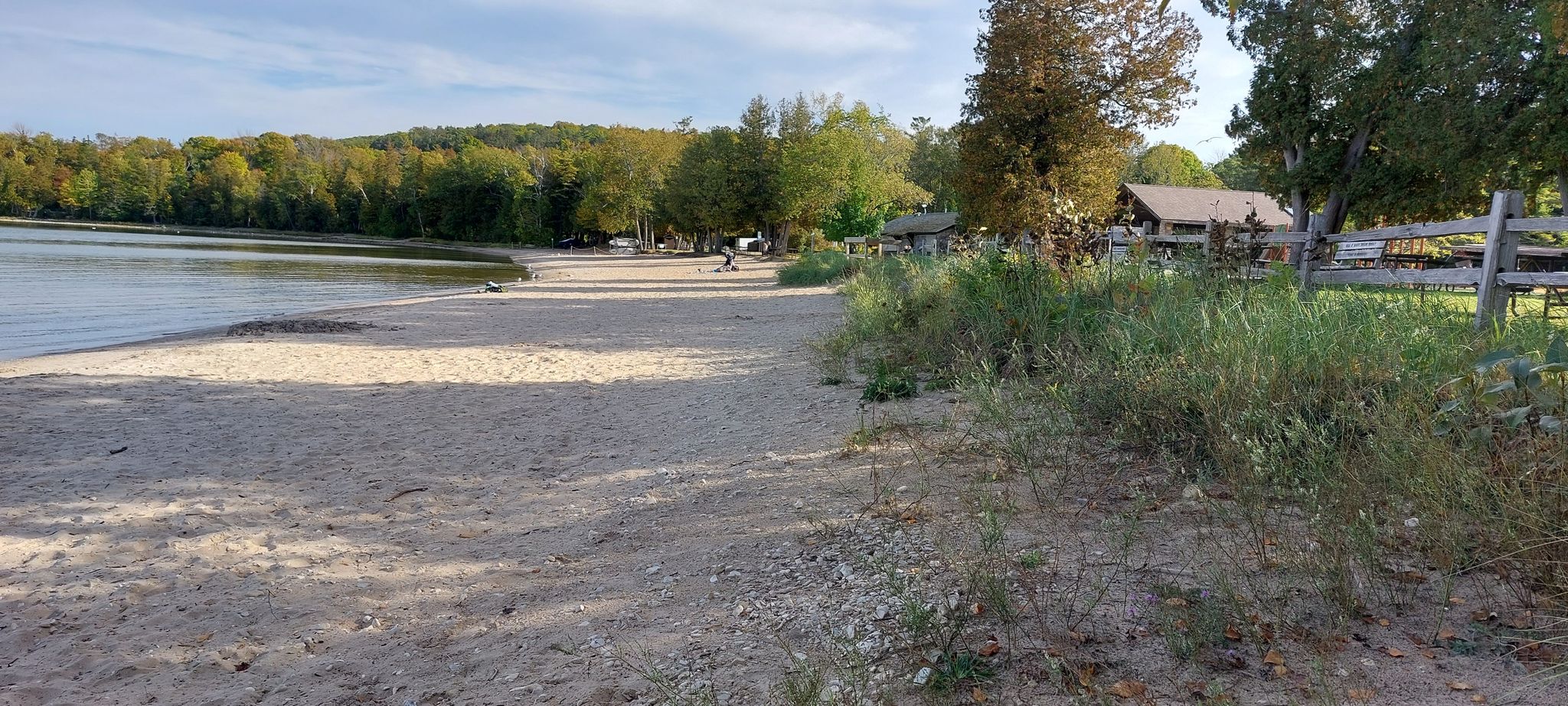 Sandy beach by a calm lake with distant buildings and green trees. - Fish Creek Public Beach loop from Eagle Bluff Lighthouse
