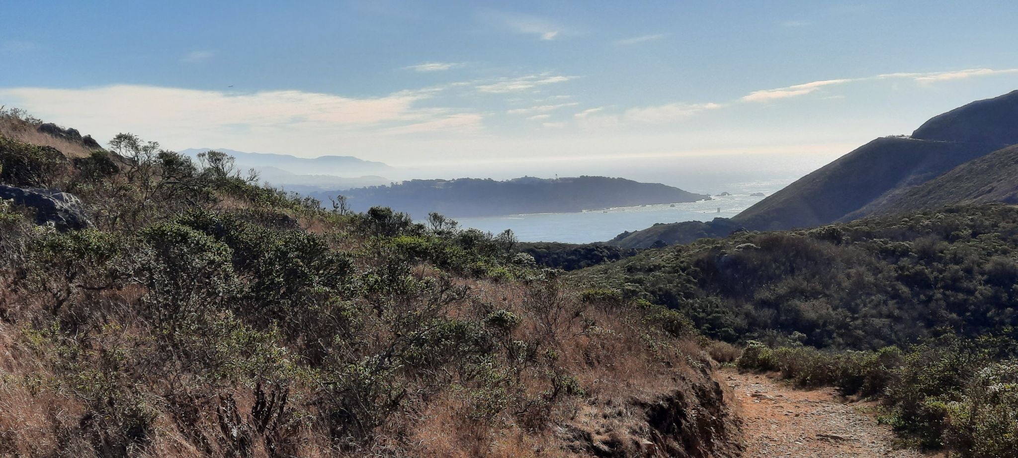 Hilly coastal landscape with dry brush overlooking a hazy bay and ocean. - Slacker Hill and Hawk Hill via Coastal Trail