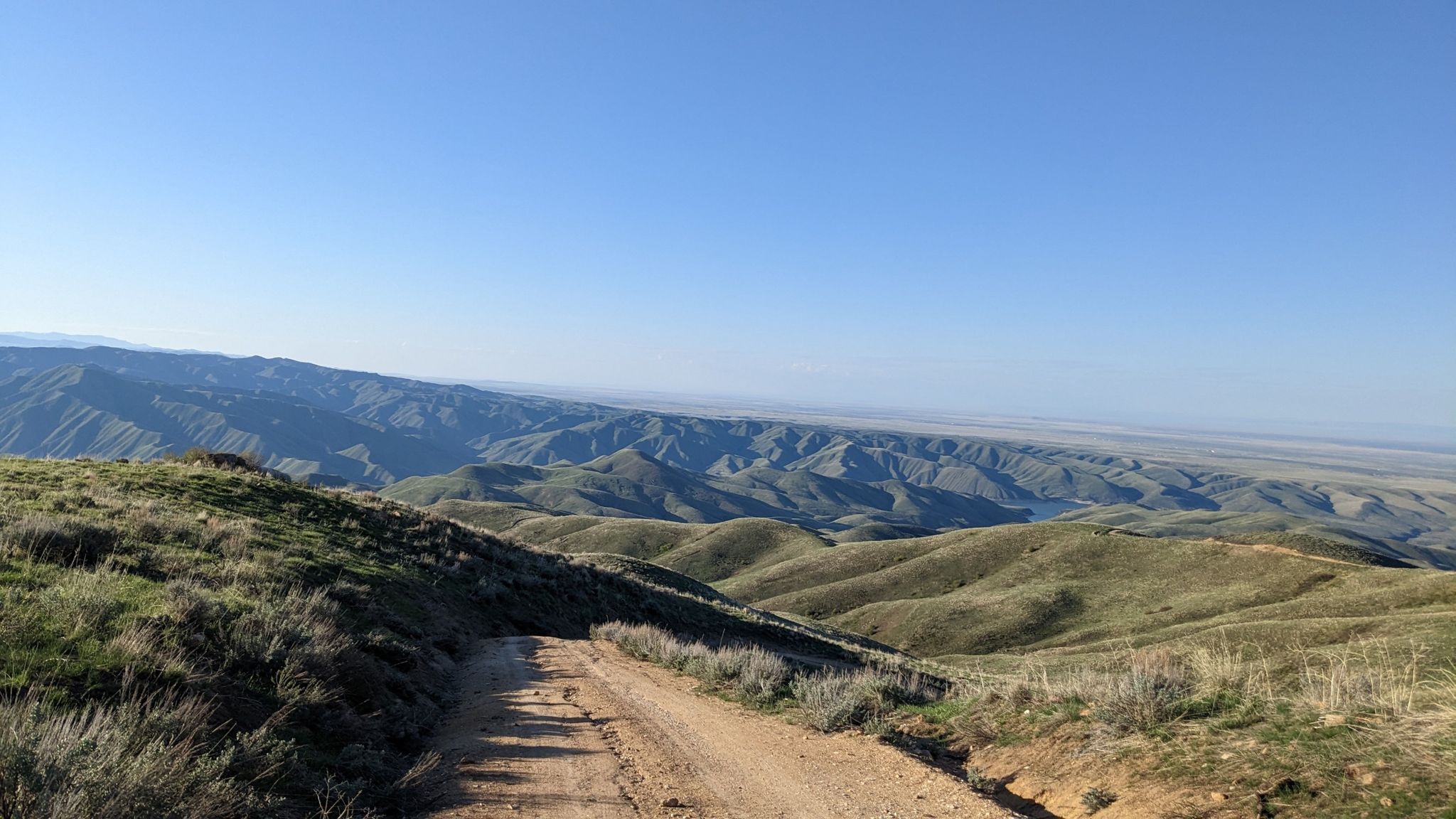 Dirt road descends through sunny, green rolling hills and distant mountains. - Shaw Mountain Road and Homestead Trail Loop