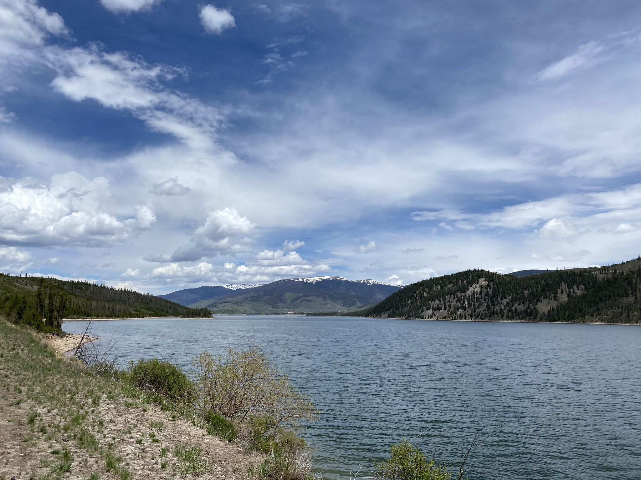 Expansive lake surrounded by forested hills and distant mountains under a cloudy sky. - View of Dillon Reservoir – Copper Mountain loop from High School
