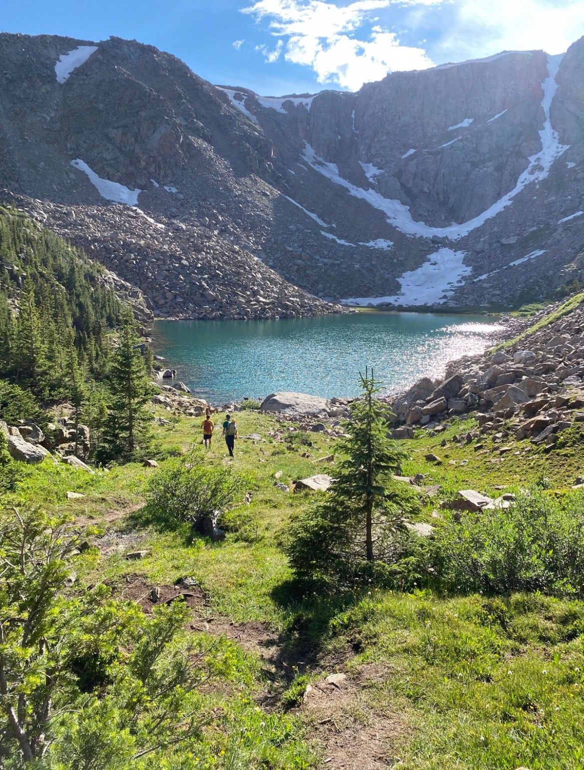 Two hikers approach a turquoise mountain lake surrounded by snowy peaks. - Saint Kevin's Lake Trail