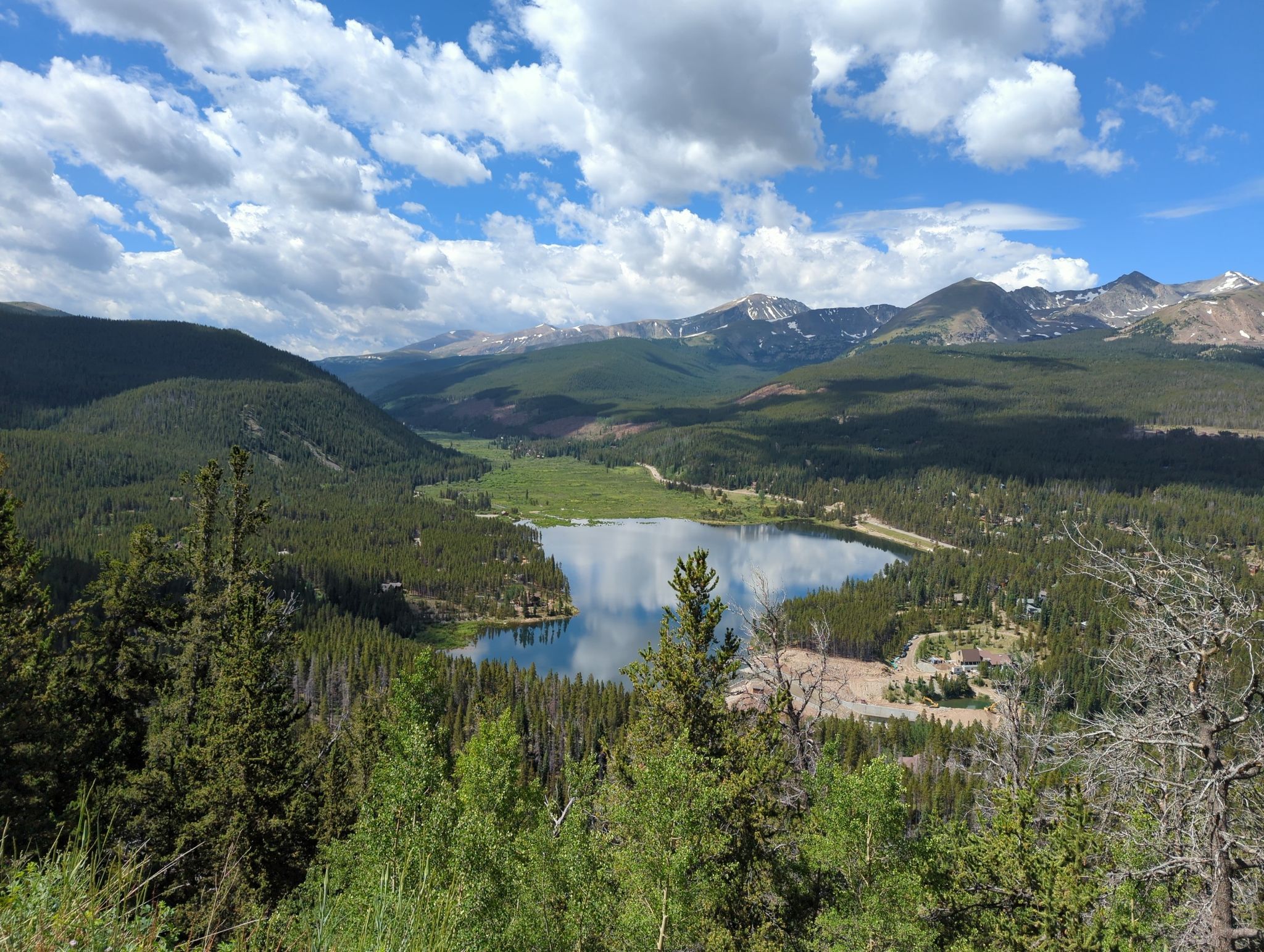 A large mountain lake surrounded by green forests, with distant peaks under a cloudy sky. - Boreas Pass Road