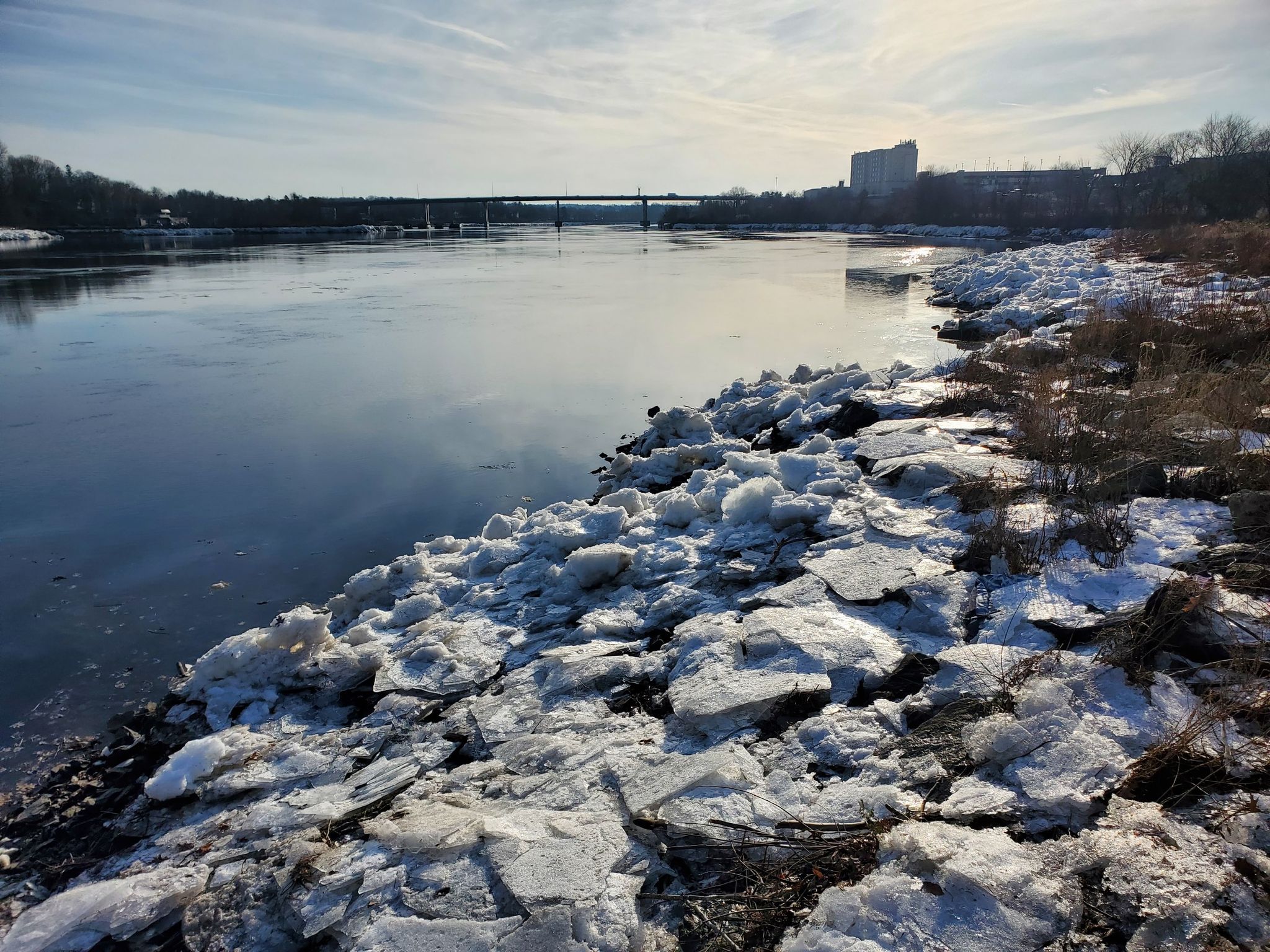 River with ice chunks on the bank, bridge in distance, bright sky. - Mann Hill and Levenseller Roads loop