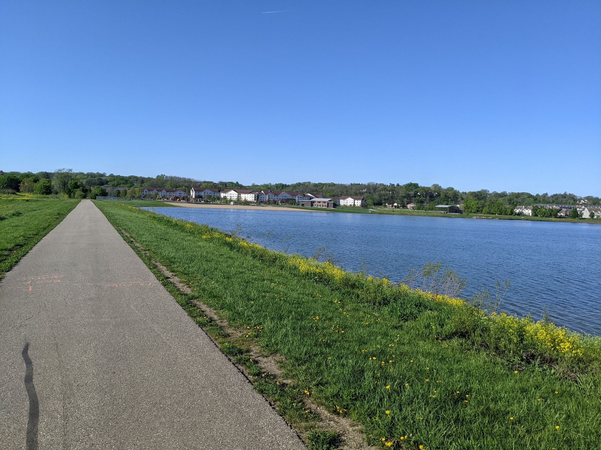 Paved path alongside a calm lake with distant houses under a clear sky. - Cascade Creek Loop Trail