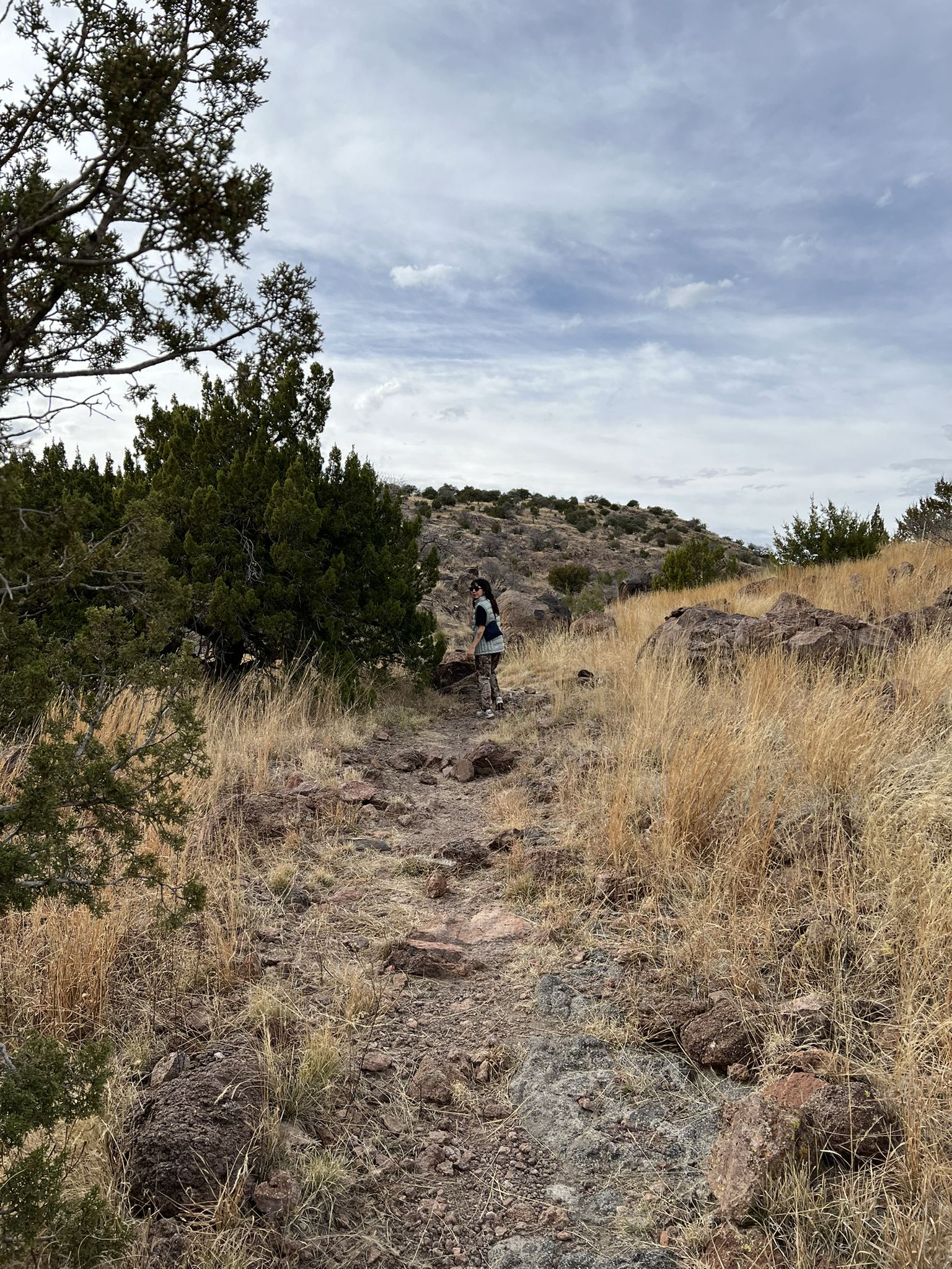 A hiker on a rocky path through dry, grassy hills under an overcast sky. - CDRI Upper Loop