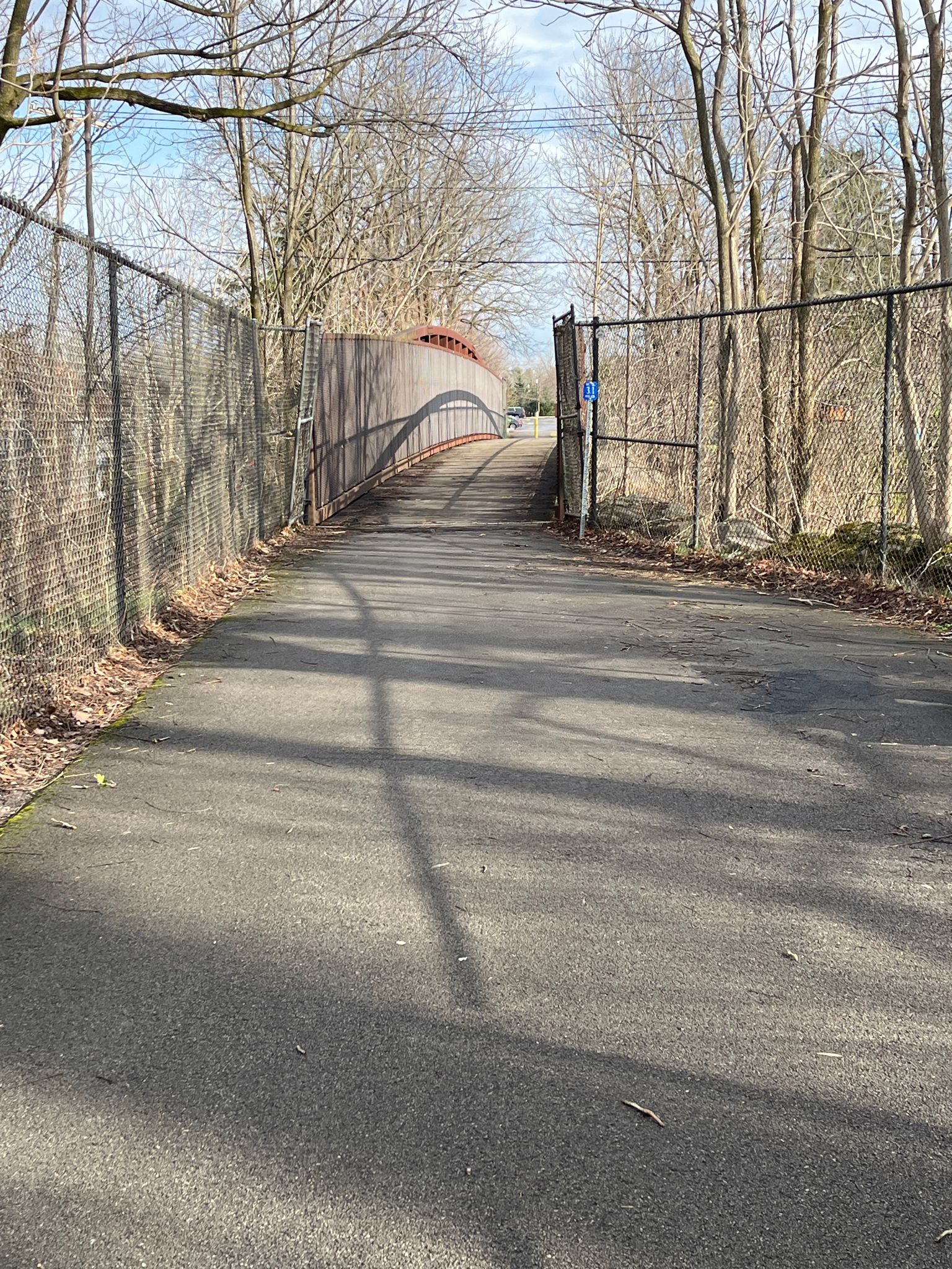 A paved path with fences on both sides leads to a red bridge. - Portable Toilet – The Brickhall loop from Village of Akron