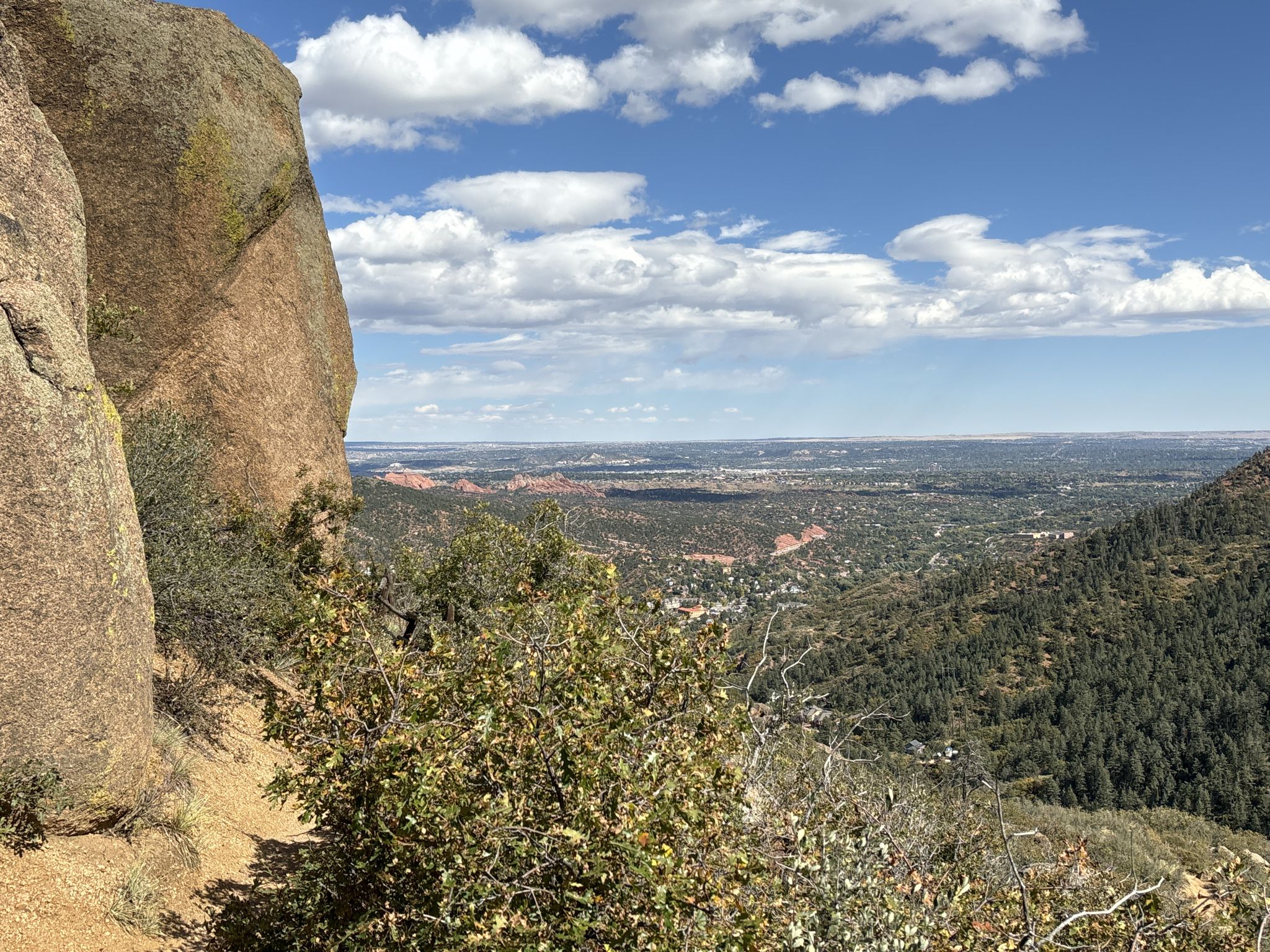 Large rock overlooks a vast valley and distant town under a cloudy sky. - Manitou Incline and Barr Trail Loop