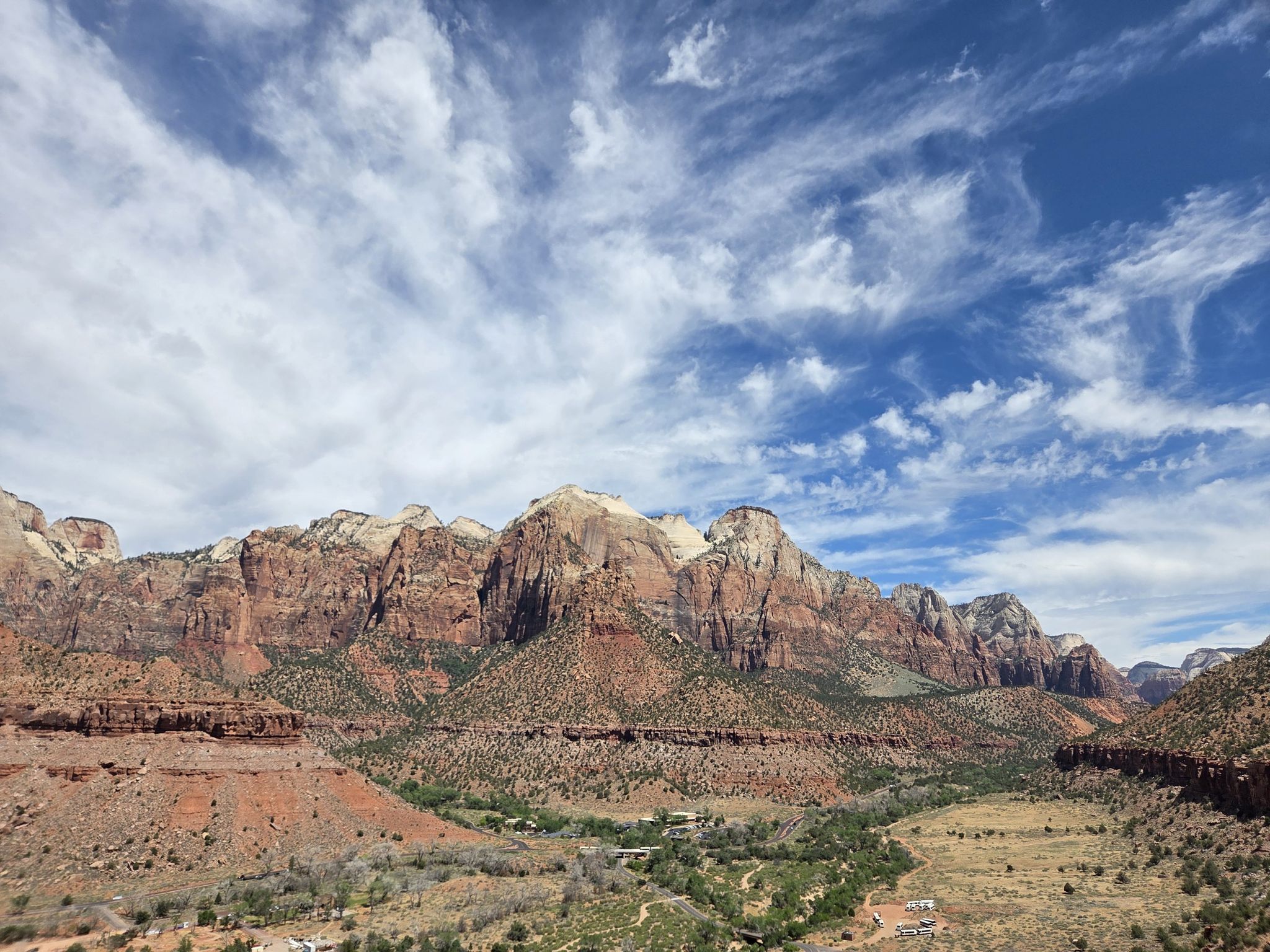 Majestic red rock mountains under a partly cloudy blue sky, with green valley below. - Watchman Trail