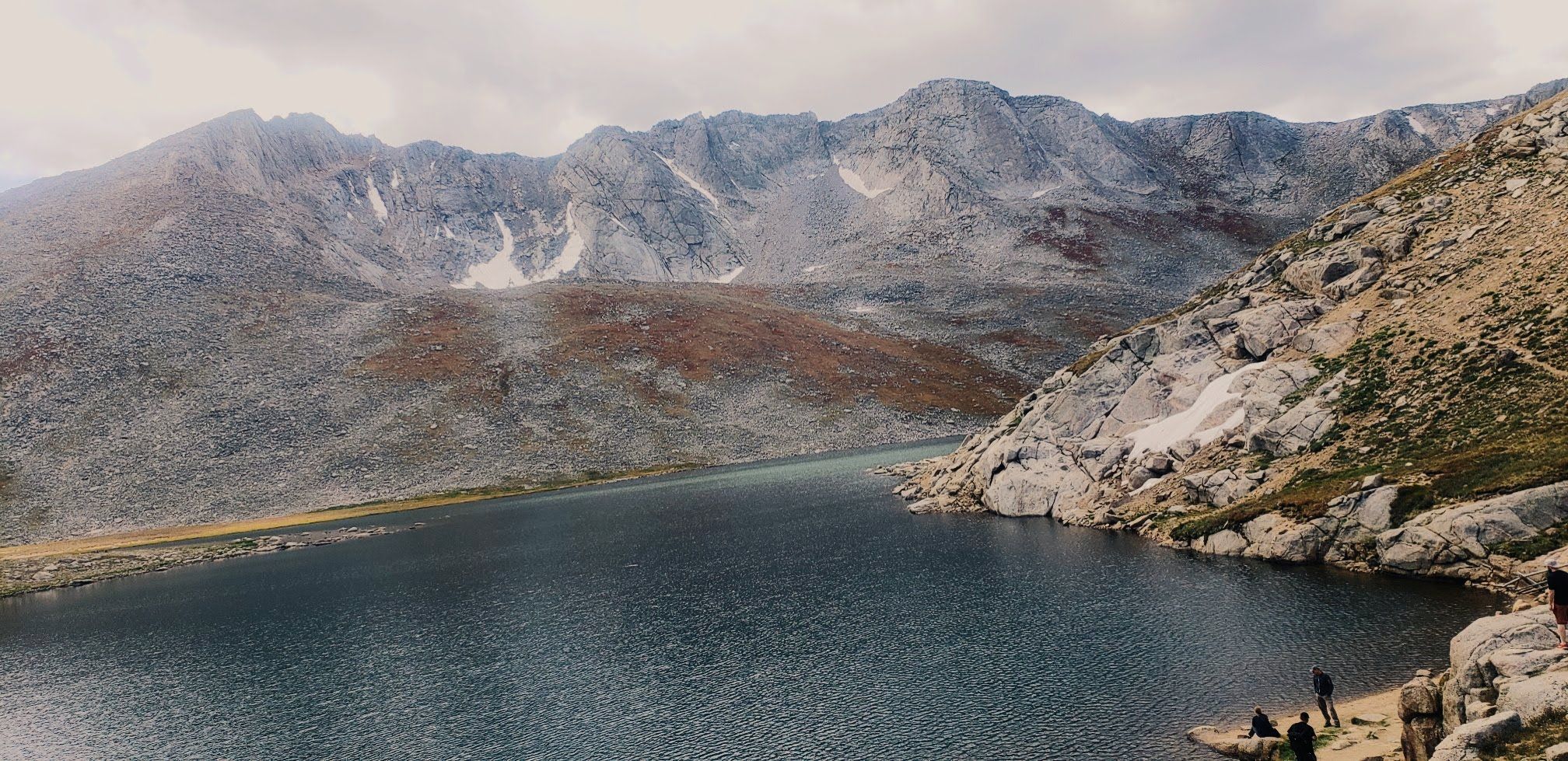 Large mountain lake with rocky shores and towering, rugged mountains under a cloudy sky. - Mount Blue Sky Ridge Trail