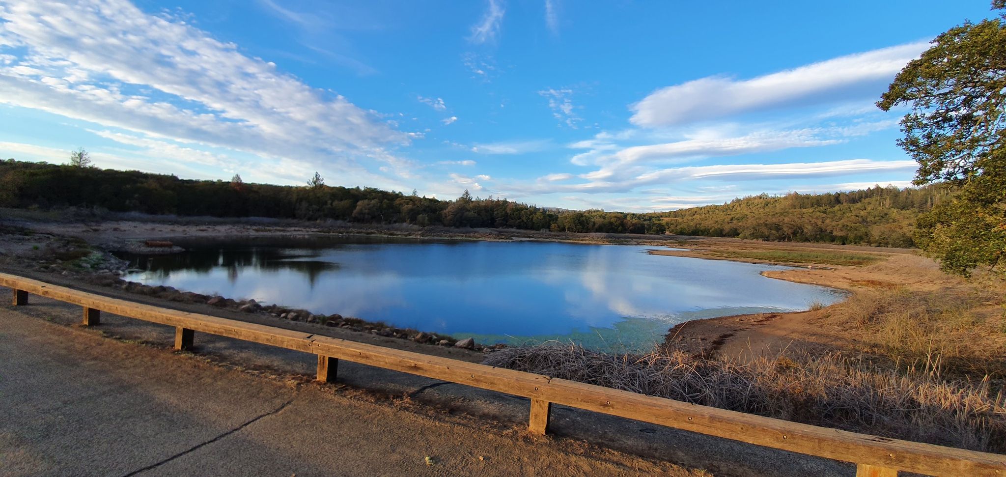 Calm lake reflecting blue sky, bordered by dry hills and a wooden fence. - Lake Ilsanjo and Buick Meadow Loop via Canyon Trail