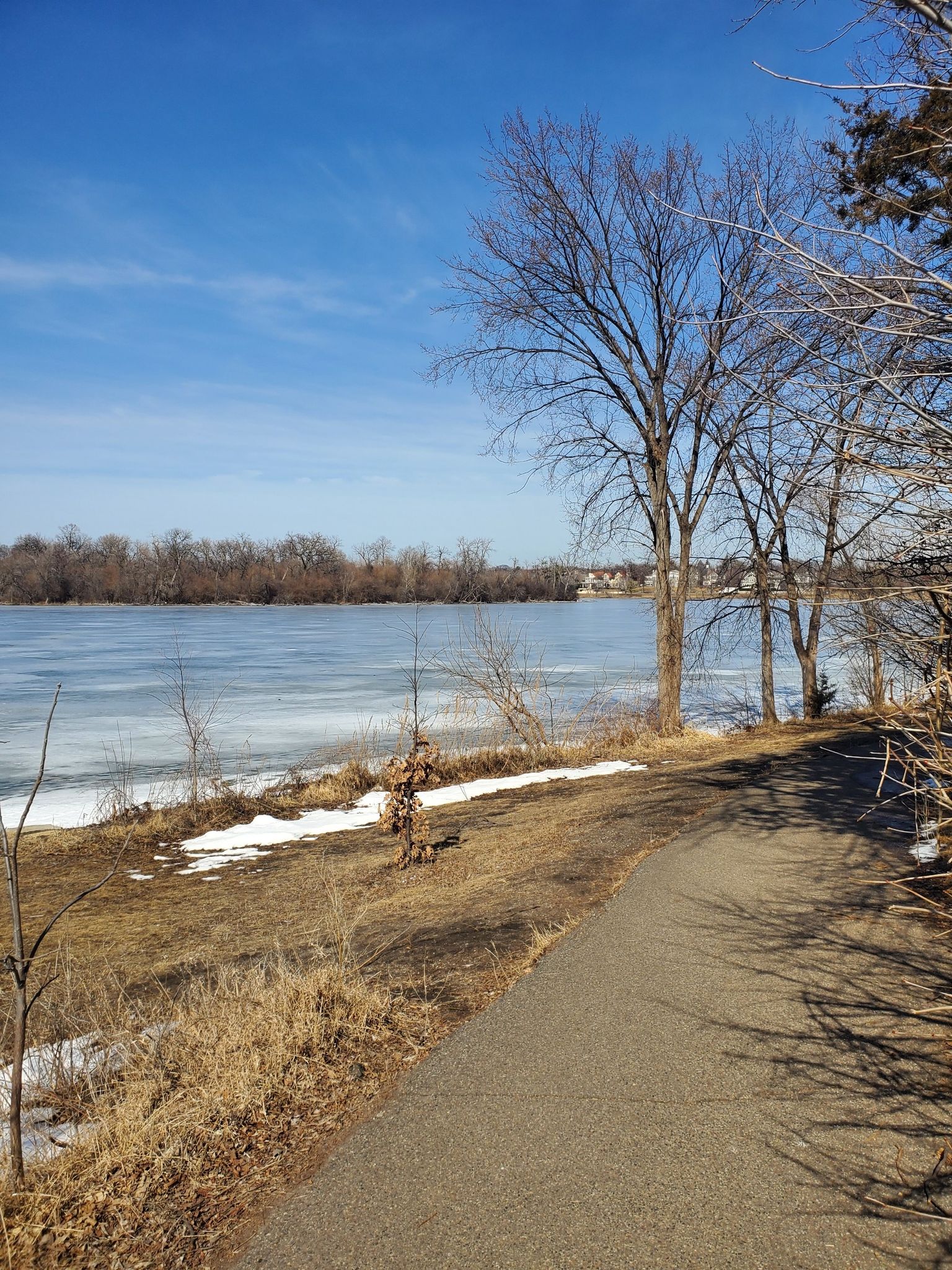 Paved path alongside a partially frozen lake with bare trees on a sunny day. - Minnesota River Bluffs Trail to Minneapolis Chain of Lakes