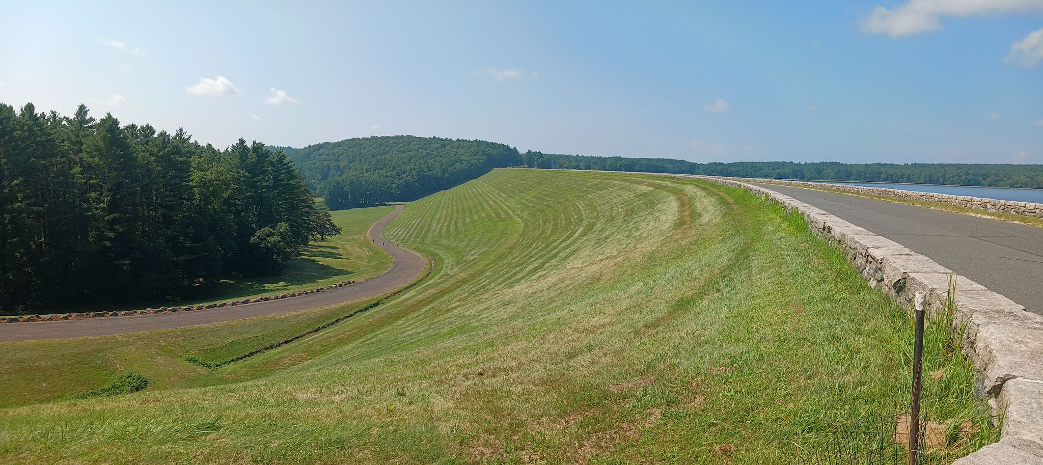 Sunny view of a wide grassy embankment next to a road and water. - Around the Quabbin Reservoir