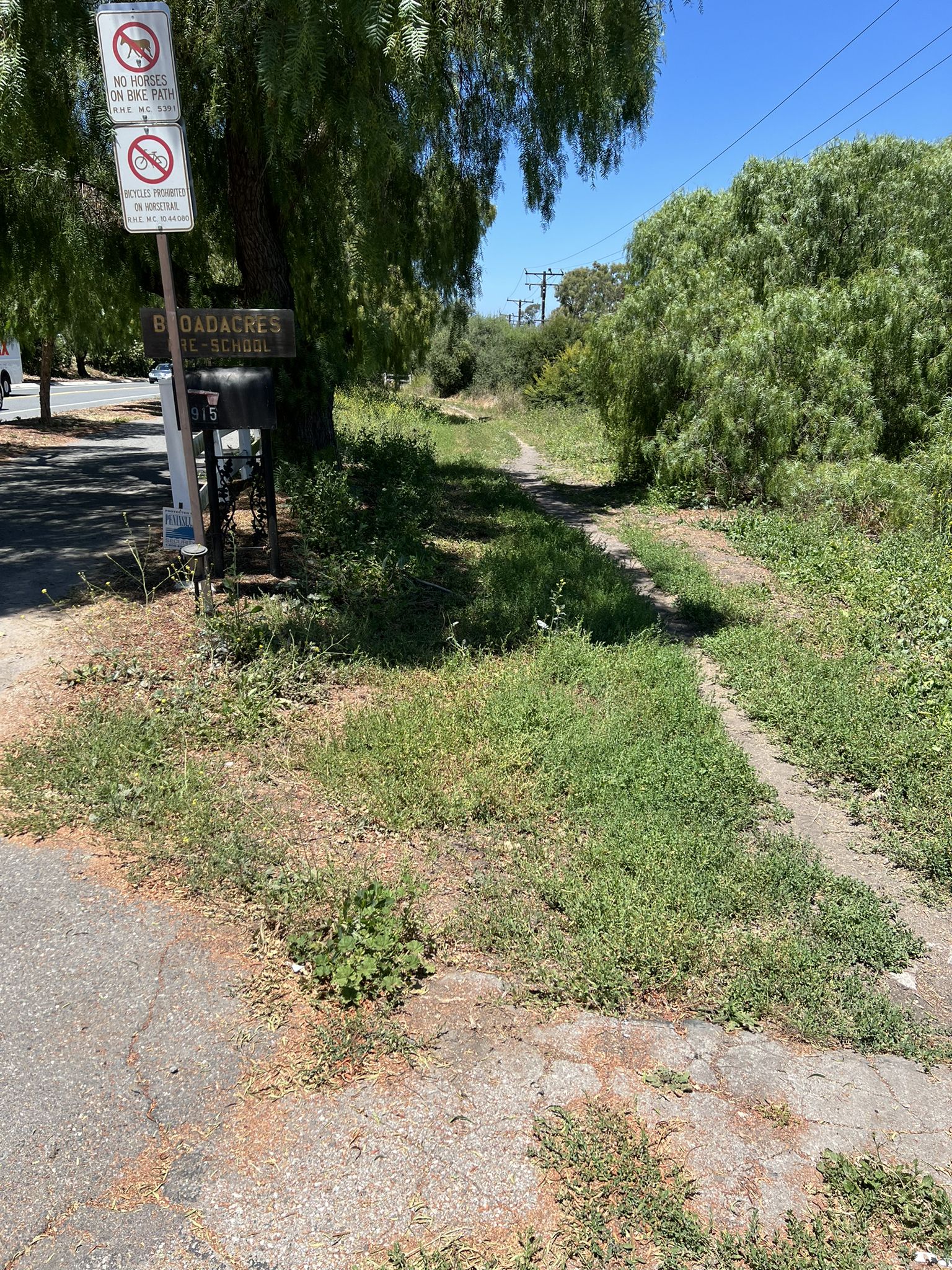 Grassy dirt path next to a paved road, sign, and lush trees. - Palos Verdes Golf Club – Via Del Monte Climb loop from Lomita