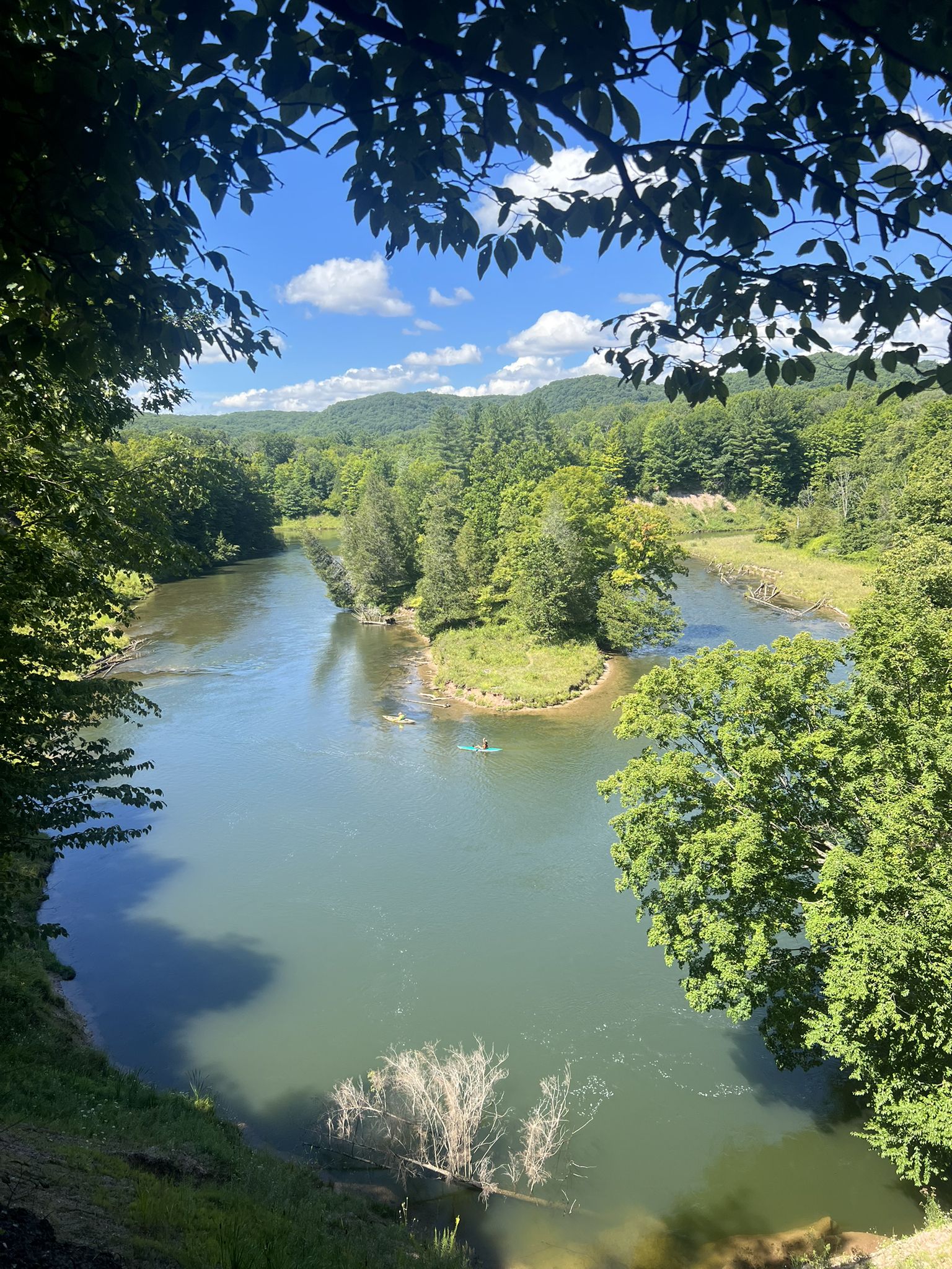 Two kayakers paddle on a river winding through a lush green forested valley. - Manistee River loop from Slagle Creek Overlook