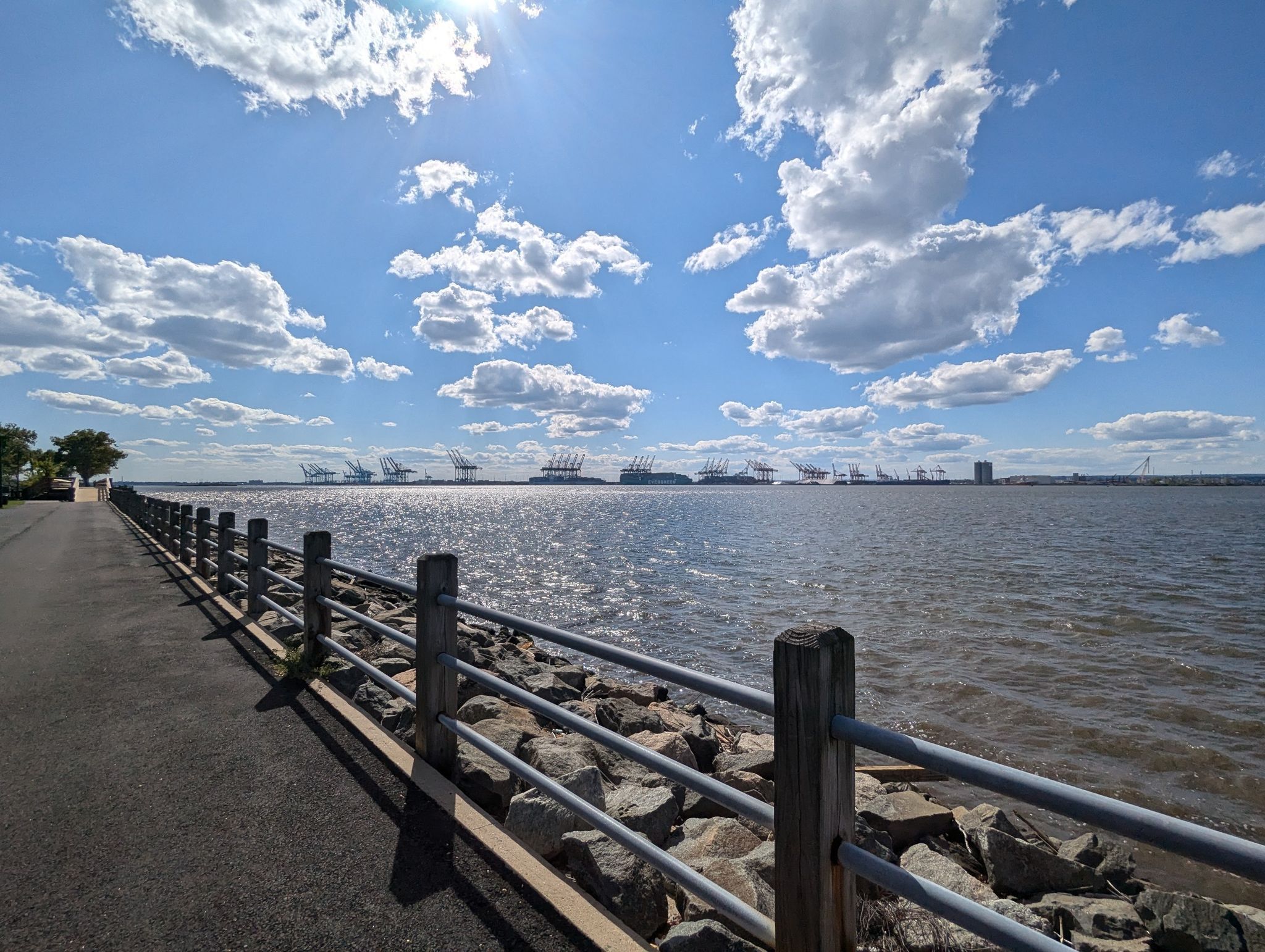 Sunny day over a wide body of water with a paved path and fence. - Stephen R. Gregg Bayonne Park Loop