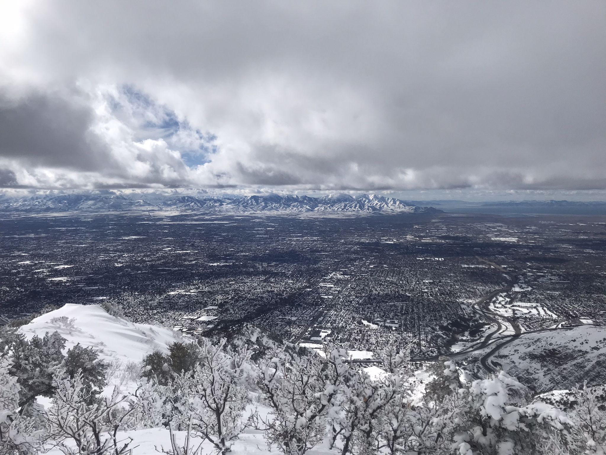 Wide snowy mountain vista with frosted trees, city below, and cloudy sky. - Grandeur Peak West Trail