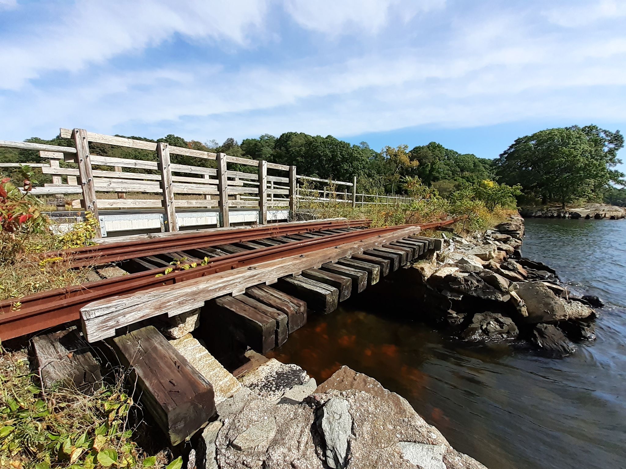 Old wooden railroad tracks over water, with a wooden fence and green foliage. - Brickyard Pond loop from East Providence