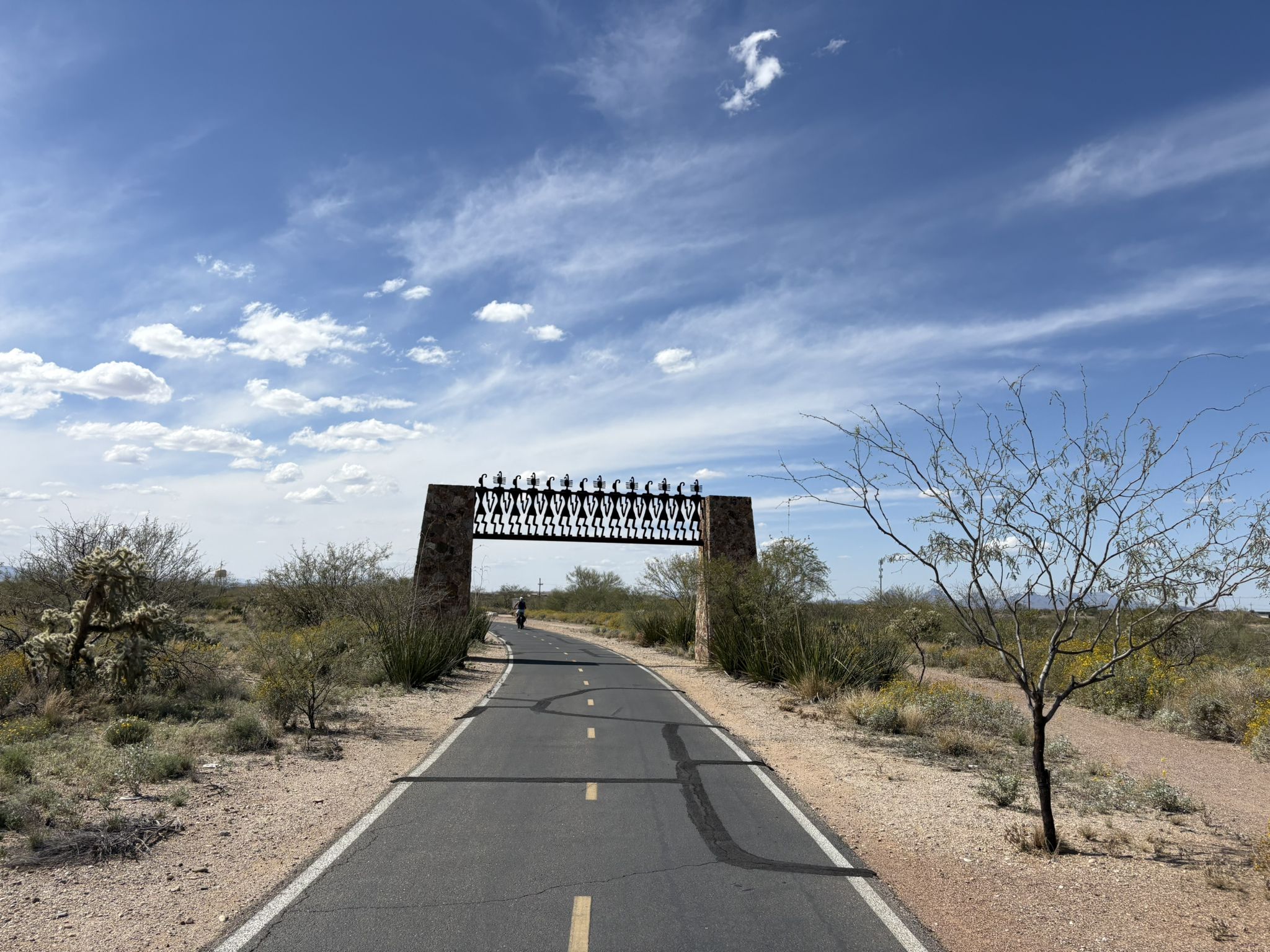 Paved path leading to a decorative stone and metal archway under a blue sky. - Robert A. Price Senior Park loop from Esmond Station