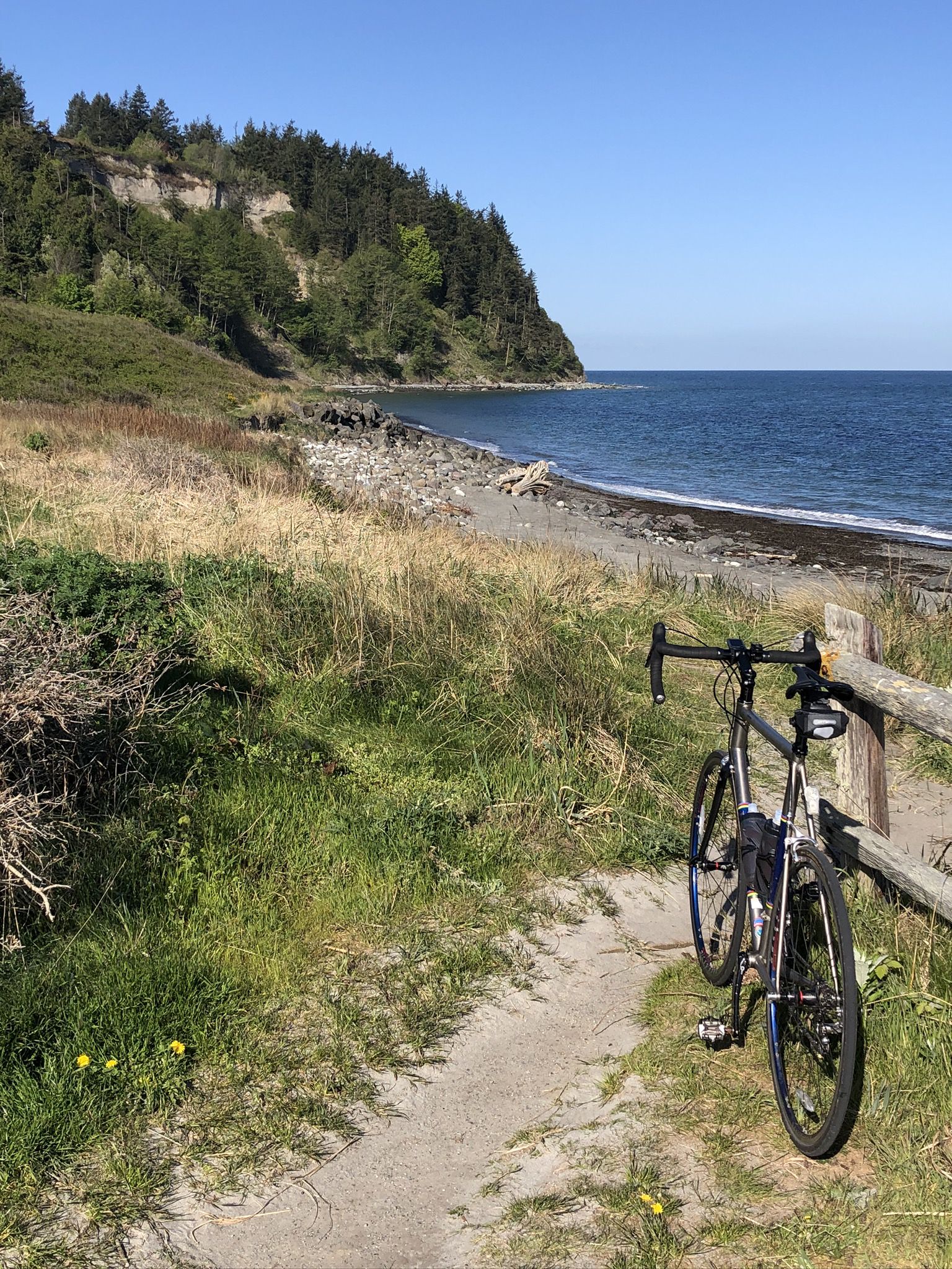 Bicycle parked on a sunny coastal path next to a rocky beach. - Point Wilson Trail