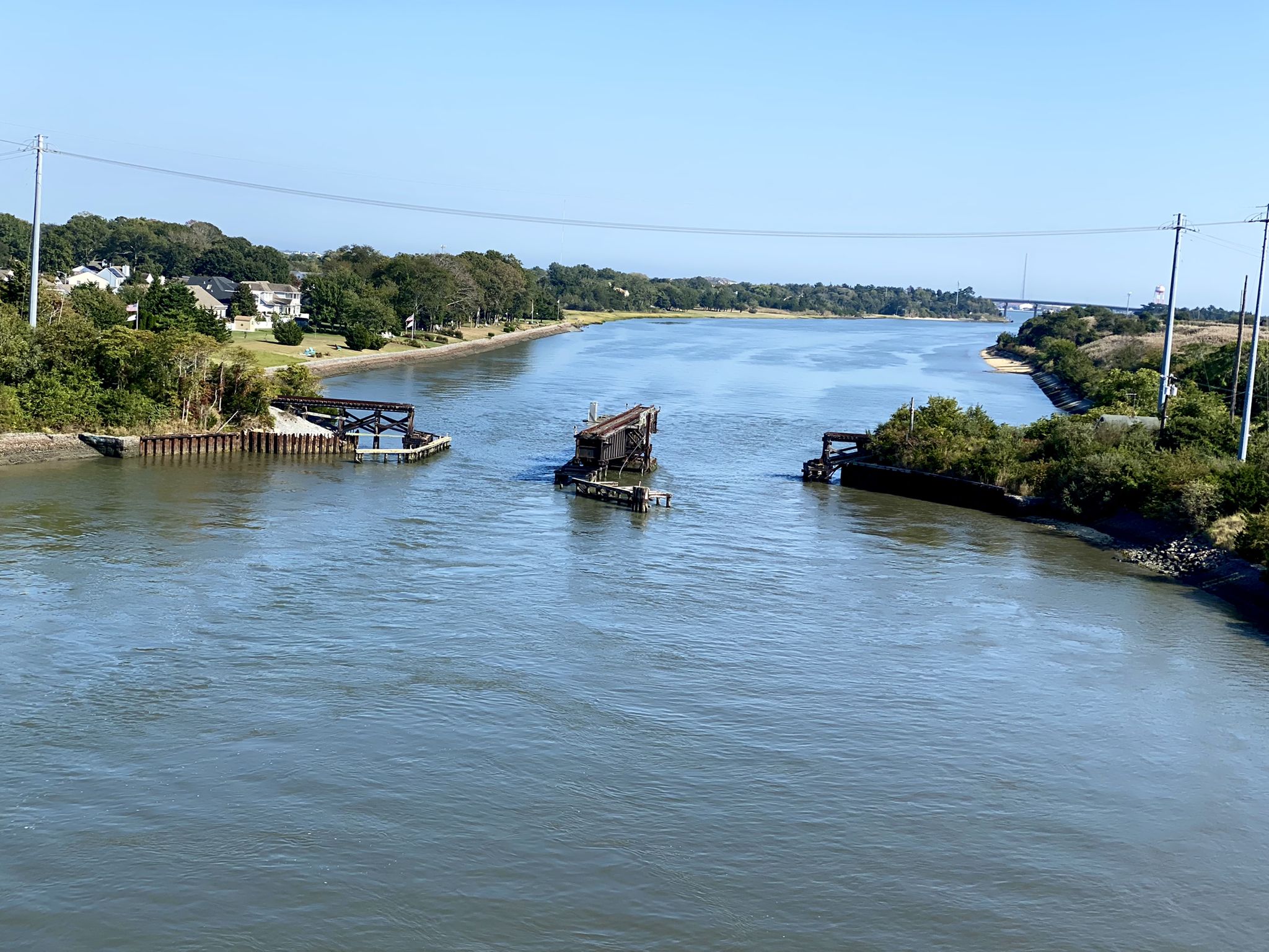 Wide river with old bridge structures under a clear blue sky. - Cape May Shoreline Ride