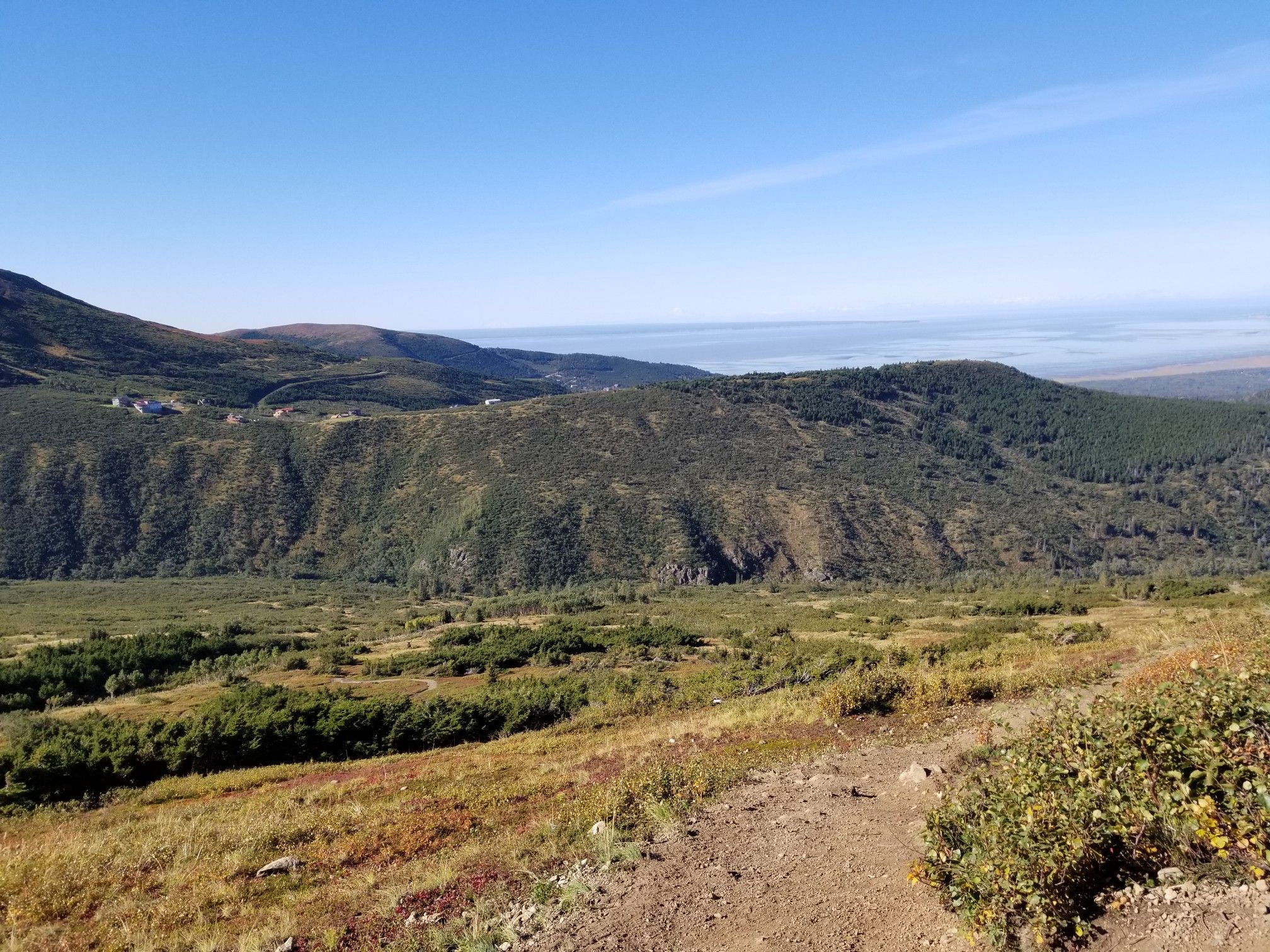 Vast mountain landscape with green hills, a dirt path, and distant water. - Peak 3 and Peak 2 Loop