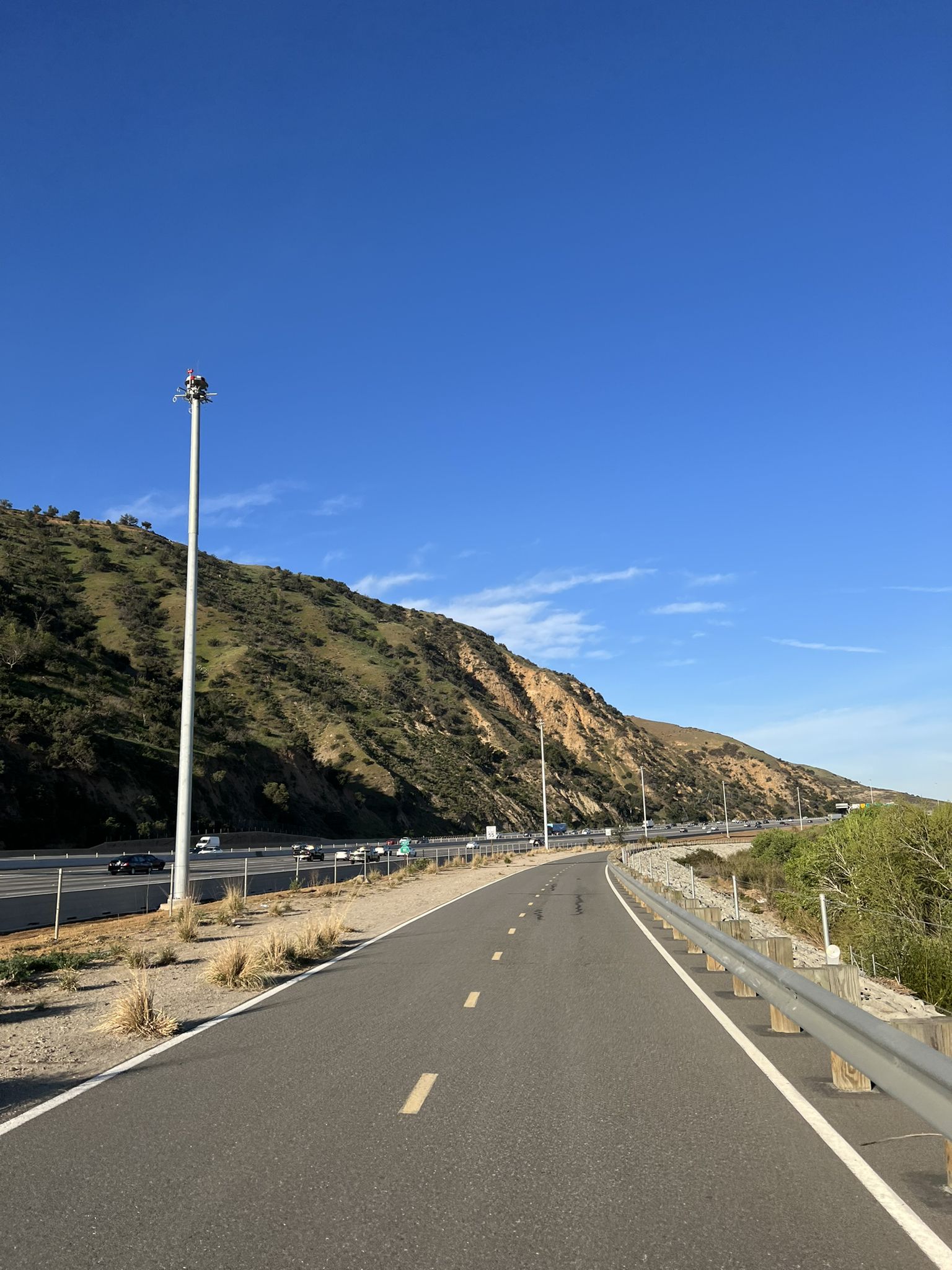 Paved road with a light pole next to a highway, winding through dry hills. - Bike loop from Fantasy Burger