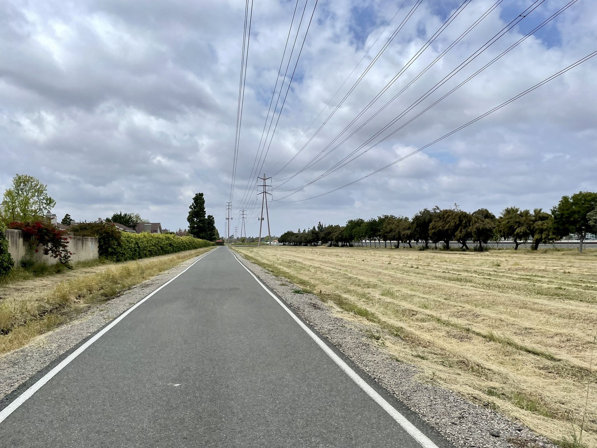 Paved path alongside a dry field with power lines under cloudy sky. - Hicks Canyon Trail – Walnut Trail loop from Championship Soccer Stadium