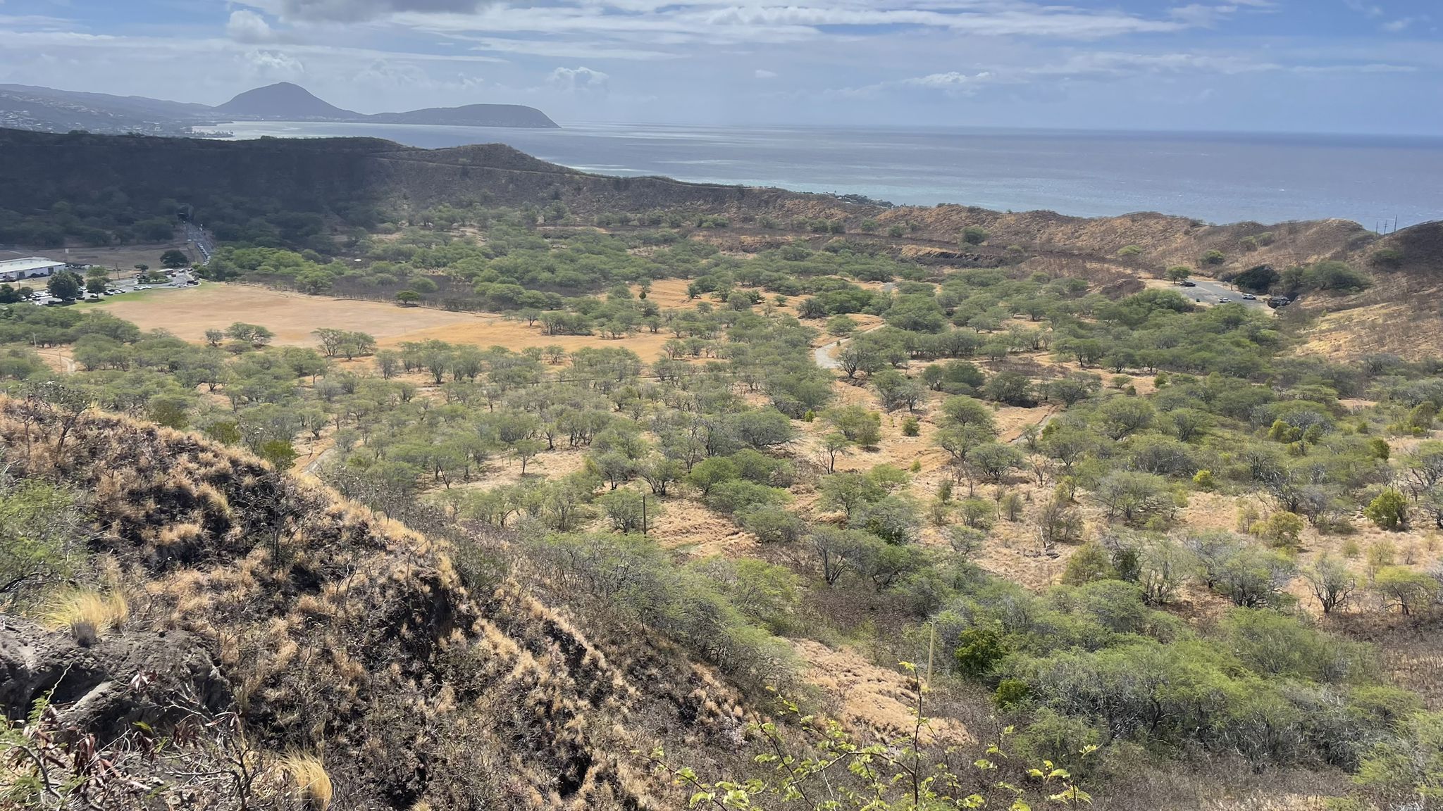 Elevated view of a dry, green valley with ocean and distant hills. - Diamond Head loop from Waikiki