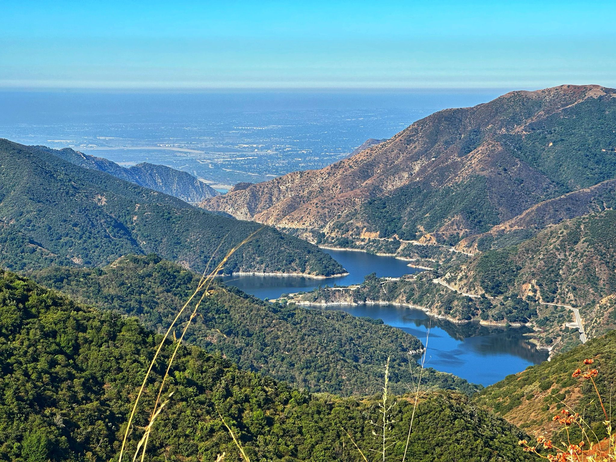 Panoramic view of a lake nestled between mountains, with a distant city. - Glendora Mountain Loop