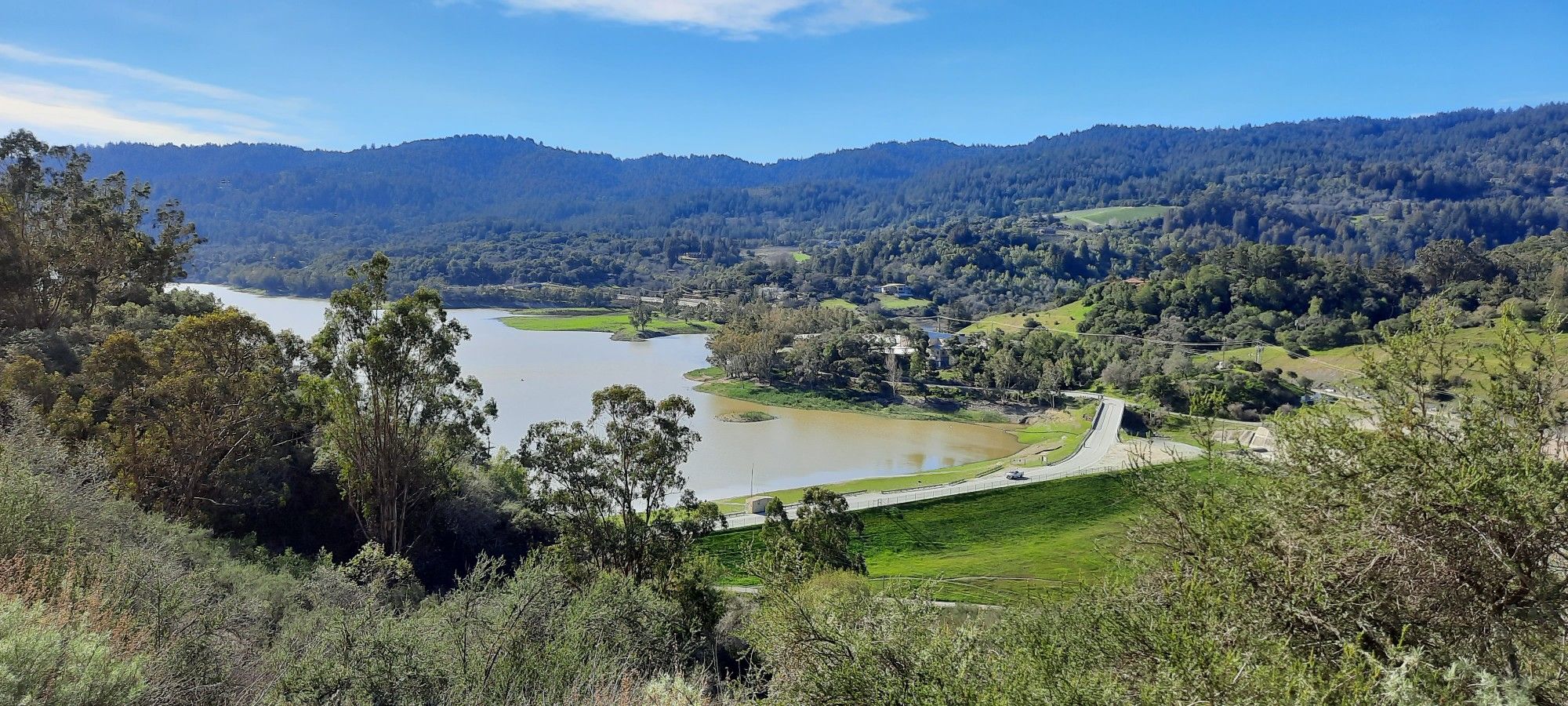 Sunny panoramic view of a lake, forested hills, and a road. - Los Gatos Creek and Jones Trail Loop