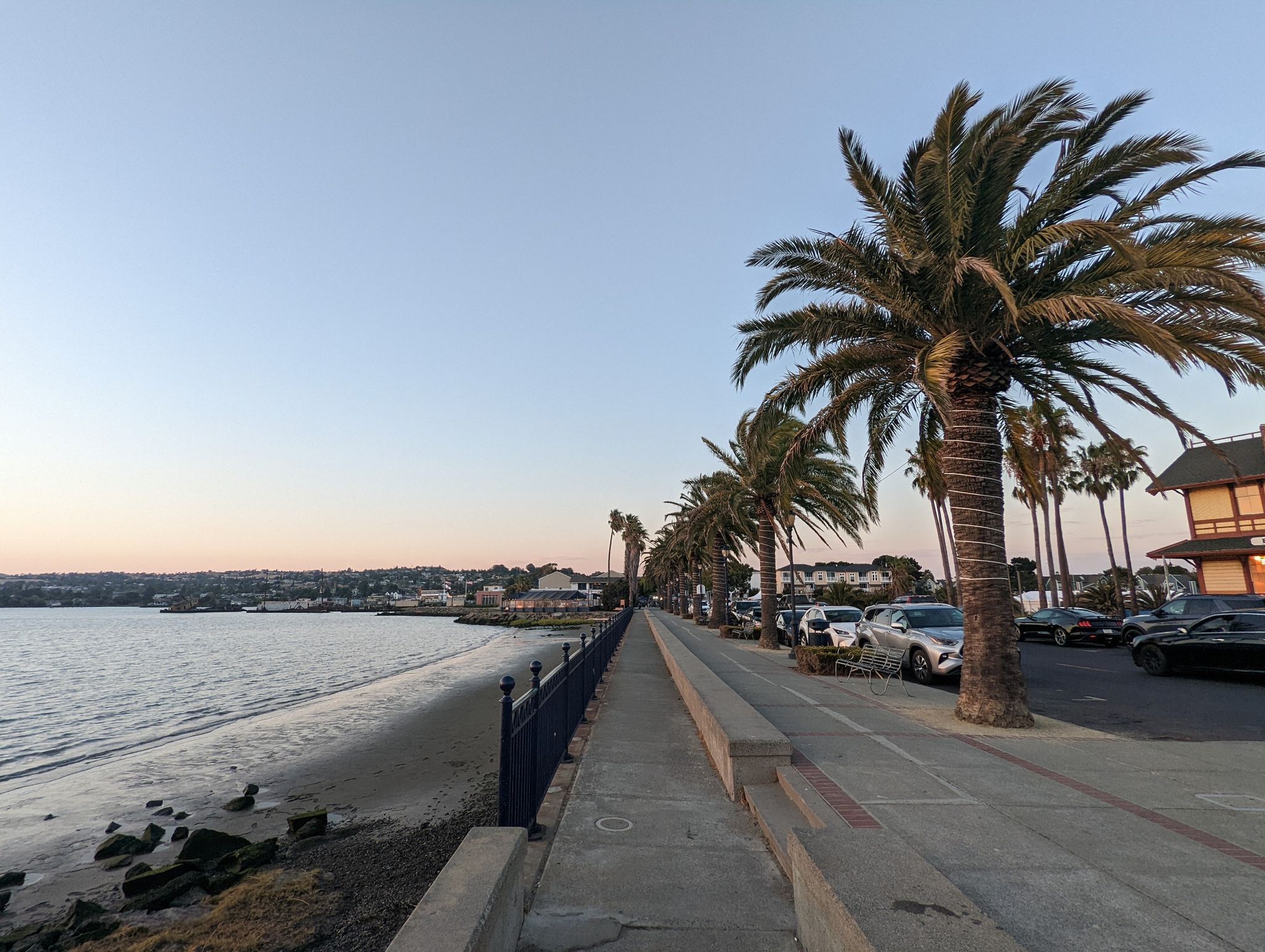 Evening view of a waterfront promenade lined with palm trees and parked cars. - Old State Capitol - Benicia – The Pony Express Memorial loop from Benicia