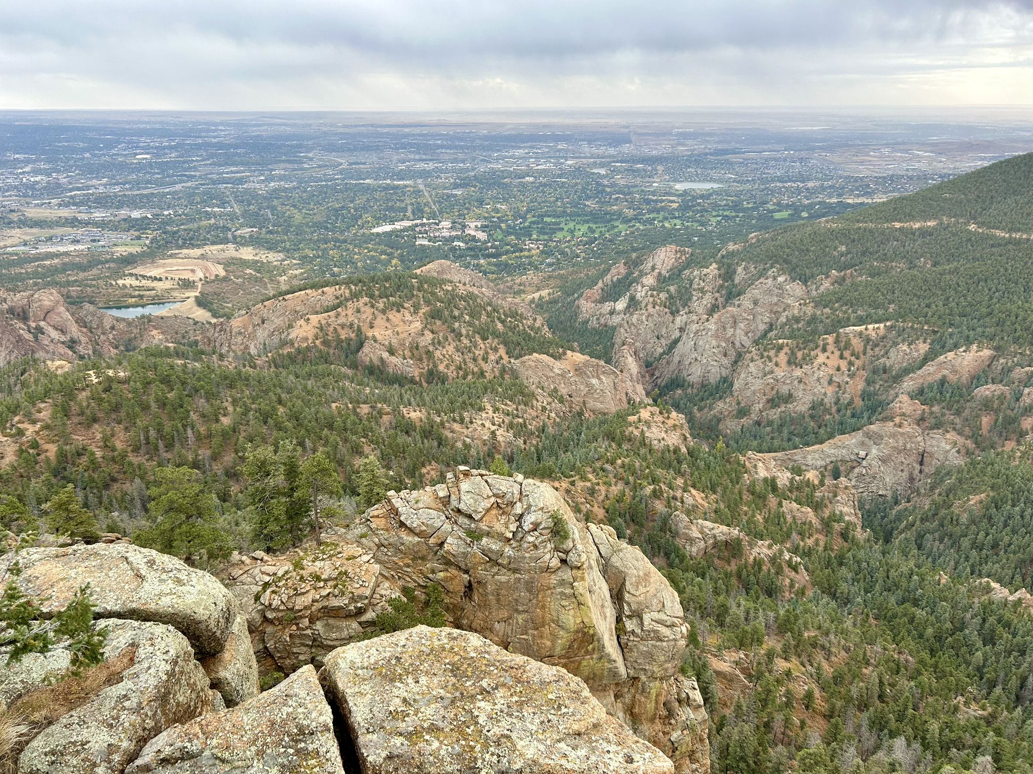 Rocky mountain vista overlooking a forested valley and distant city under cloudy skies. - Helen Hunt Falls – Mount Muscoco loop from North Cheyenne Cañon Park