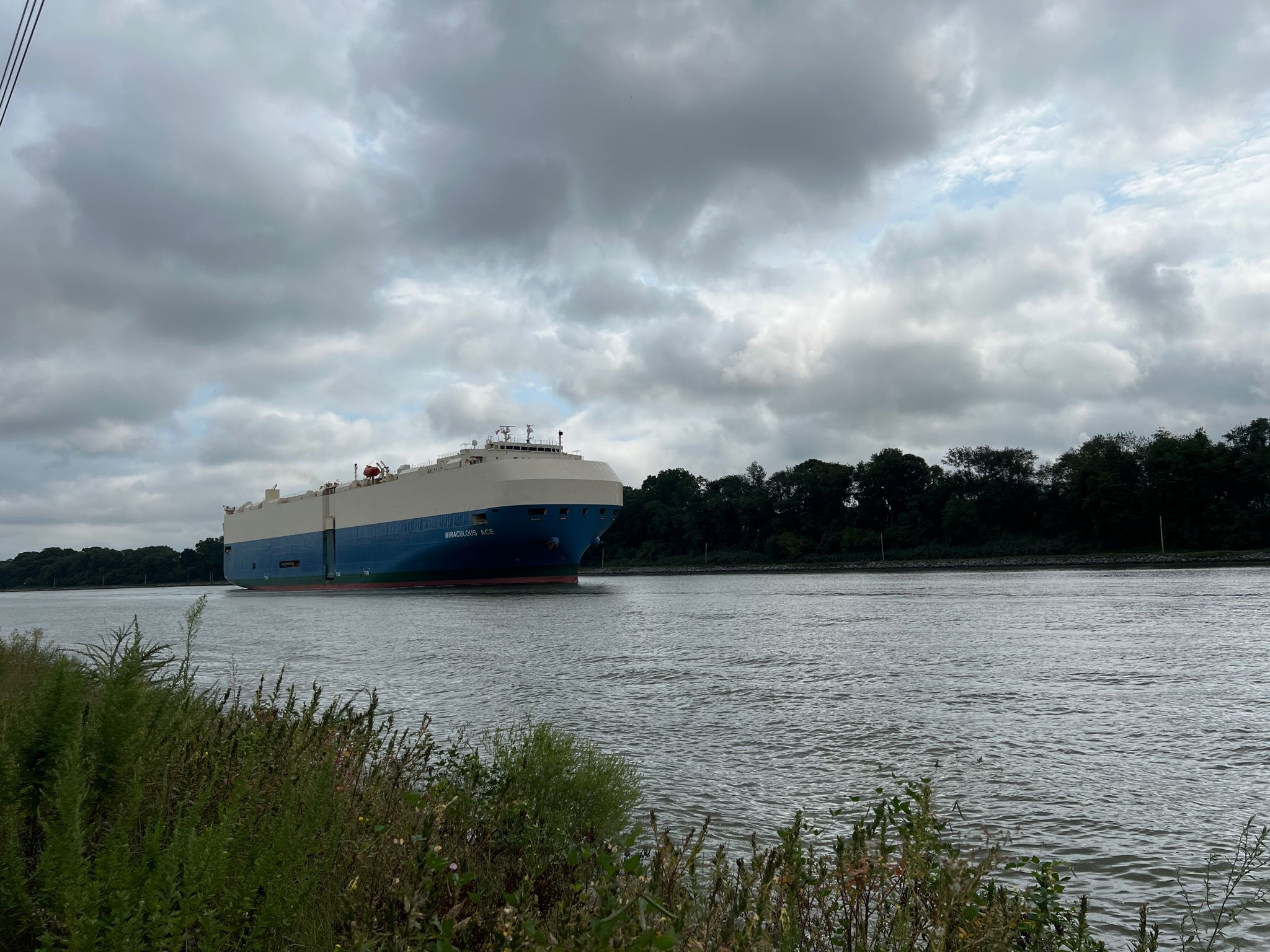 A large blue and white cargo ship moves on a river under cloudy skies. - Veterans Memorial Flagpoles – Mike Castle Trail loop from White Hall
