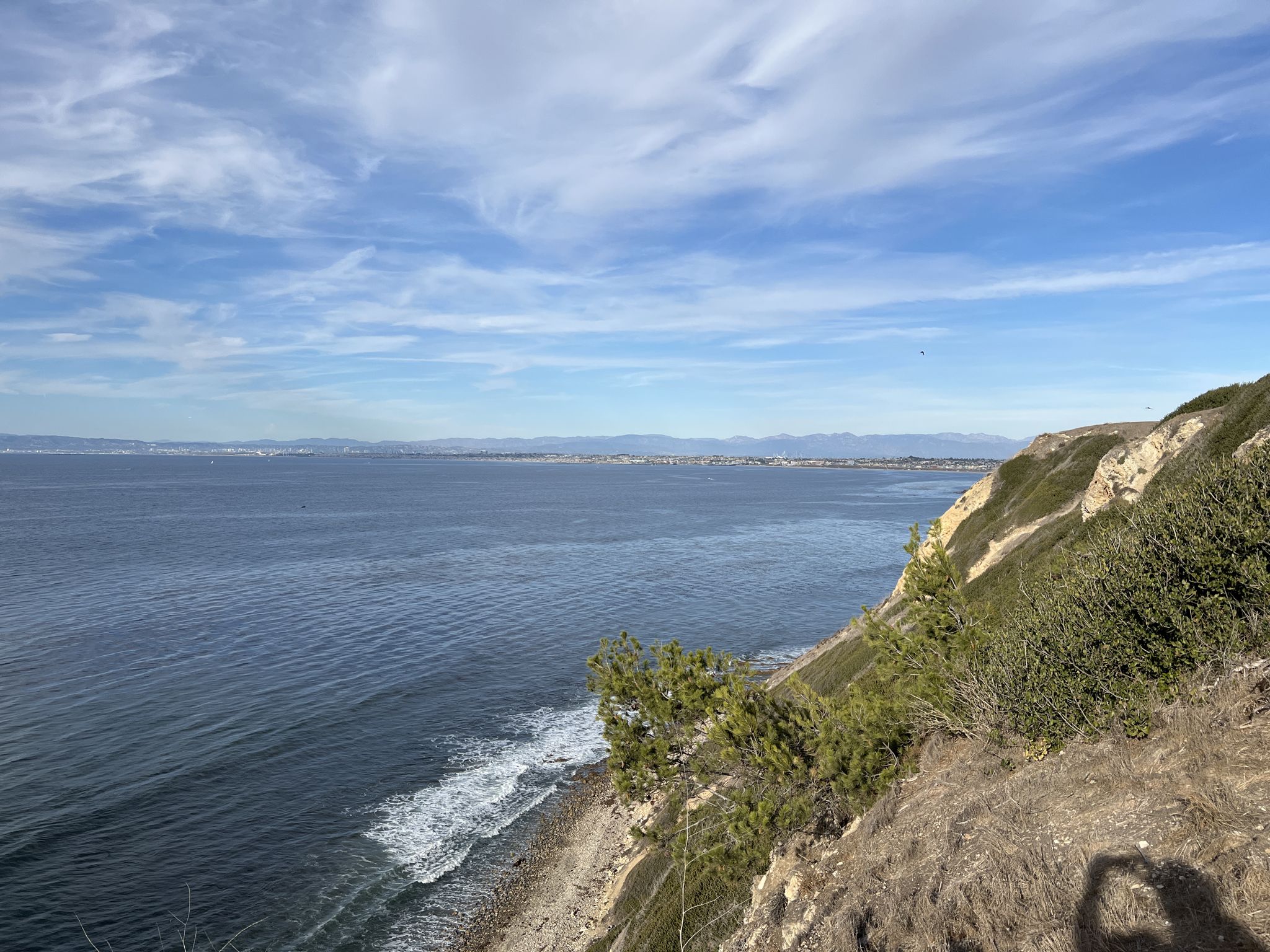 Bright coastal view with blue ocean, breaking waves, cliffs, and a person's shadow. - Paseo Del Mar Bluffs: Palos Verdes Estates Shoreline Preserve