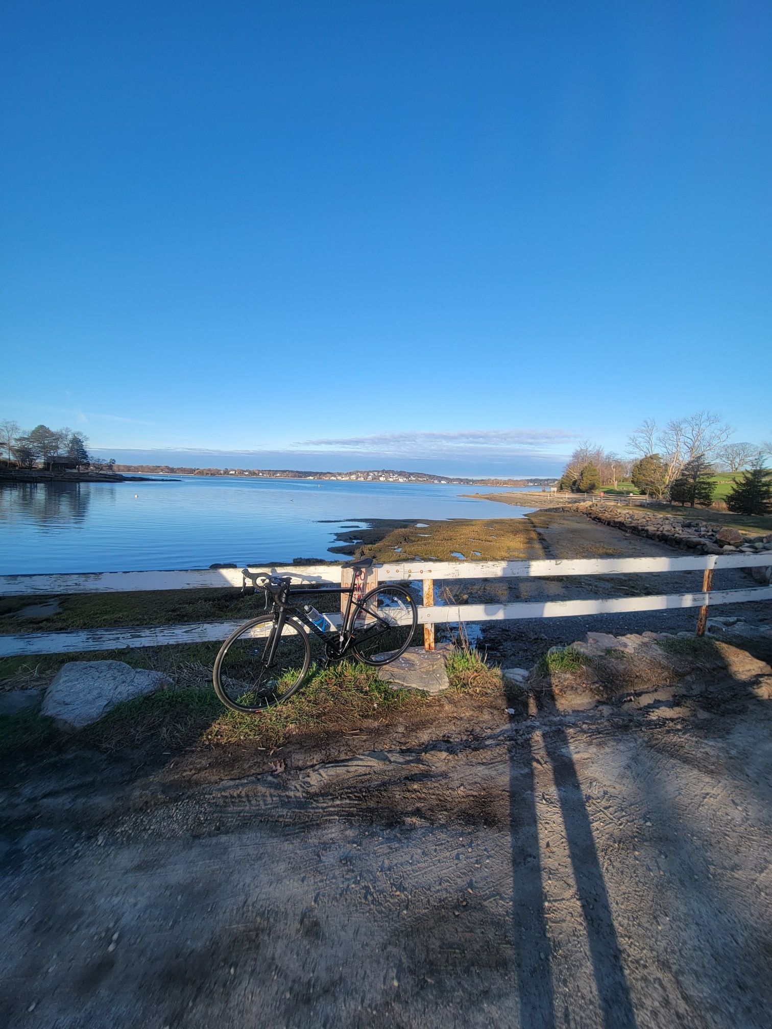 A bicycle leans on a white fence overlooking calm water on a sunny day. - Wompatuck State Park – World's End loop from South Weymouth
