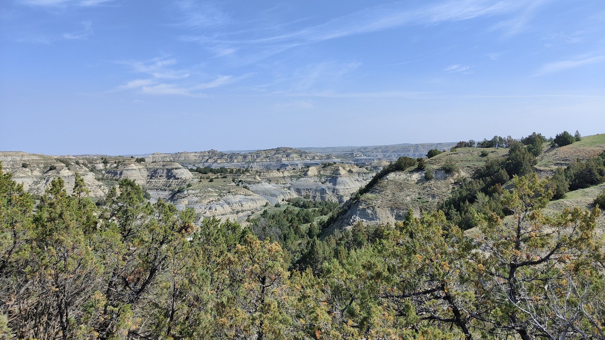 Expansive view of arid, layered hills and green valleys under a blue sky. - Caprock Coulee Trail