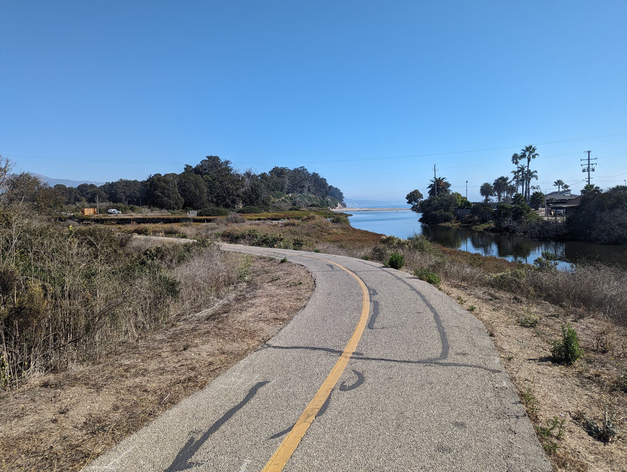 Curving paved path alongside a calm river with trees under a clear sky. - Obern Trail Loop