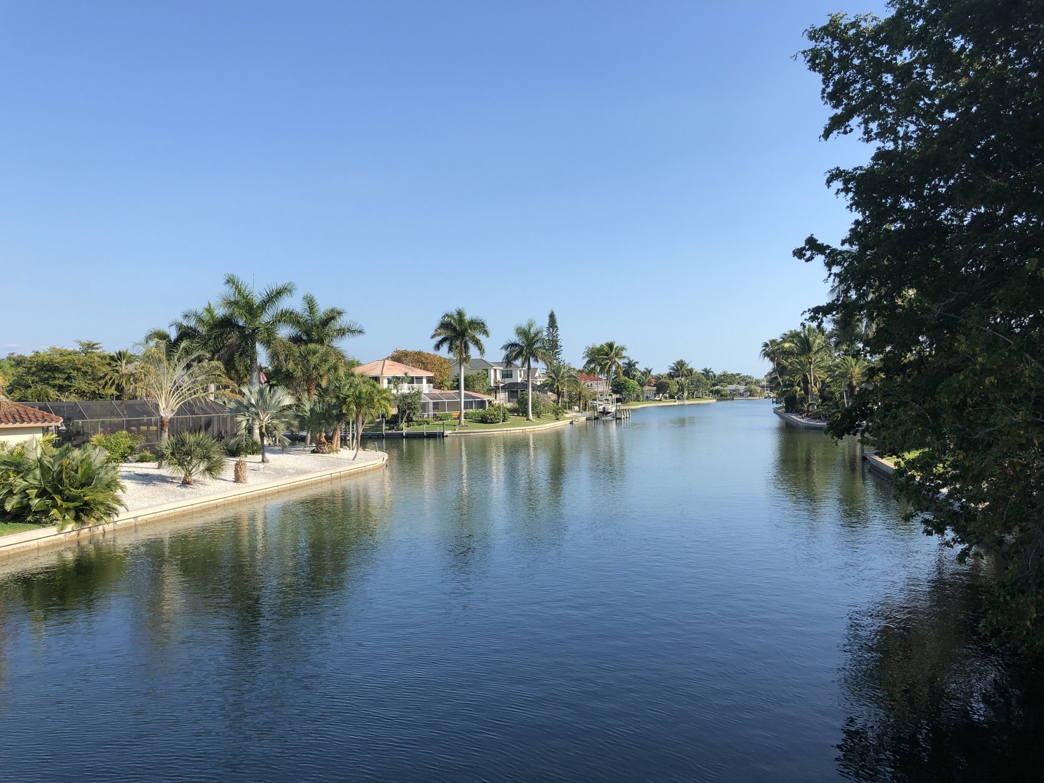 Wide canal with houses, palm trees, and clear blue sky. - Sanibel Island Bike Path – Blind Pass Bridge loop from Albright Key