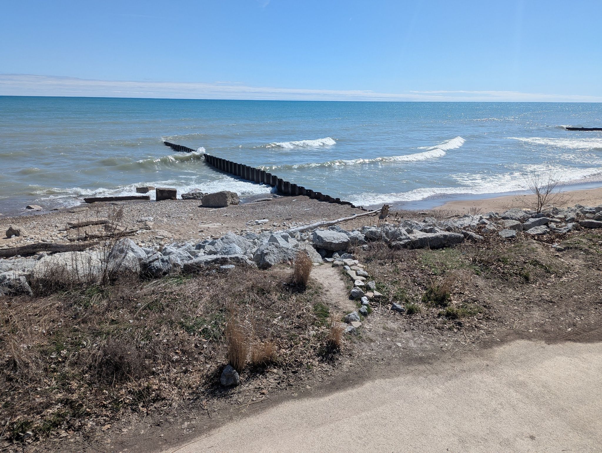 Sunny beach with waves, a wooden pier, and rocky shore. - Fort Sheridan Pond loop from Great Lakes