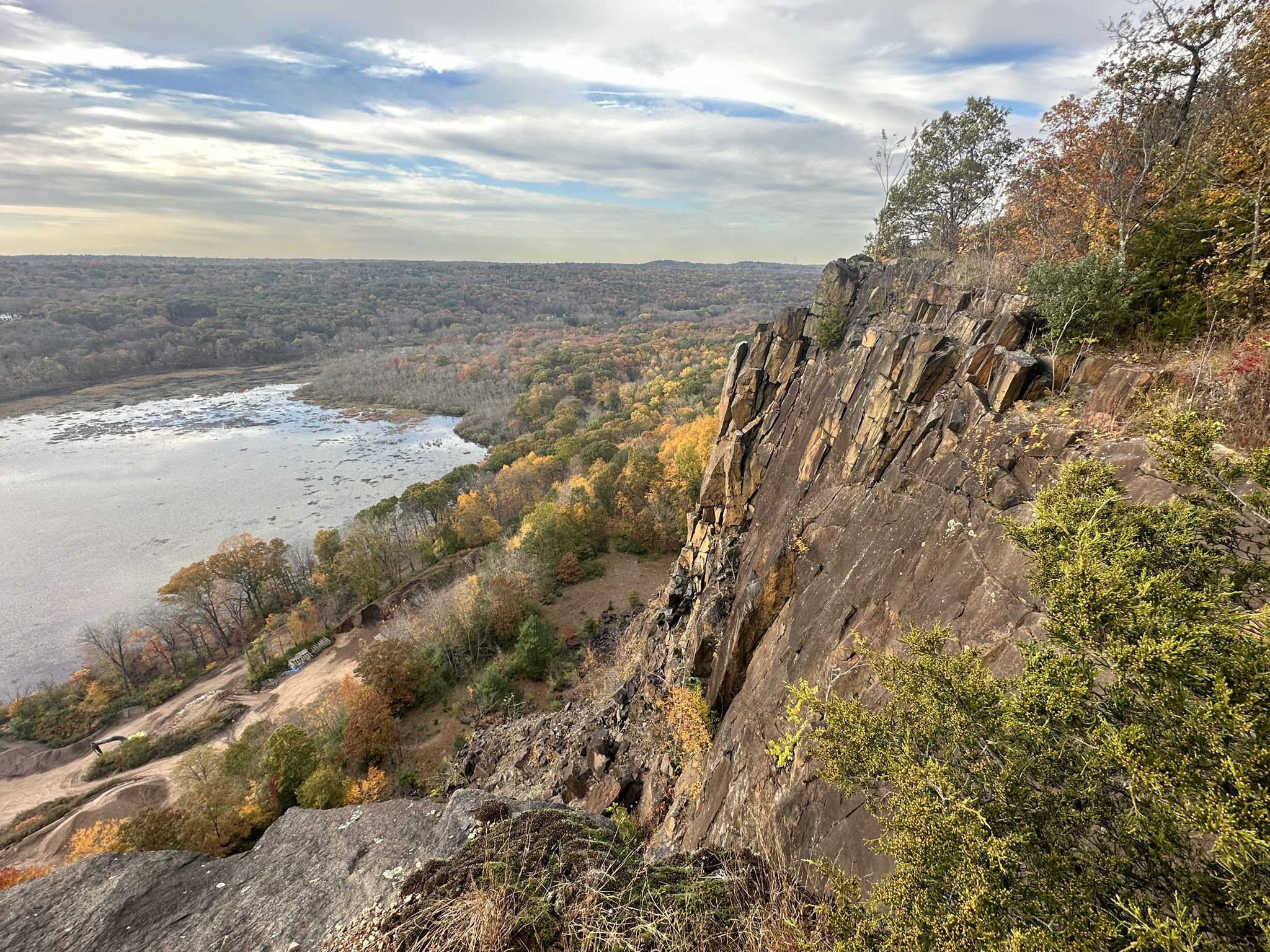 Rocky cliff overlooking a river and autumn forest under a cloudy sky. - Climb Baldwin Drive – West Rock Ridge State Park loop from Yale Bowl