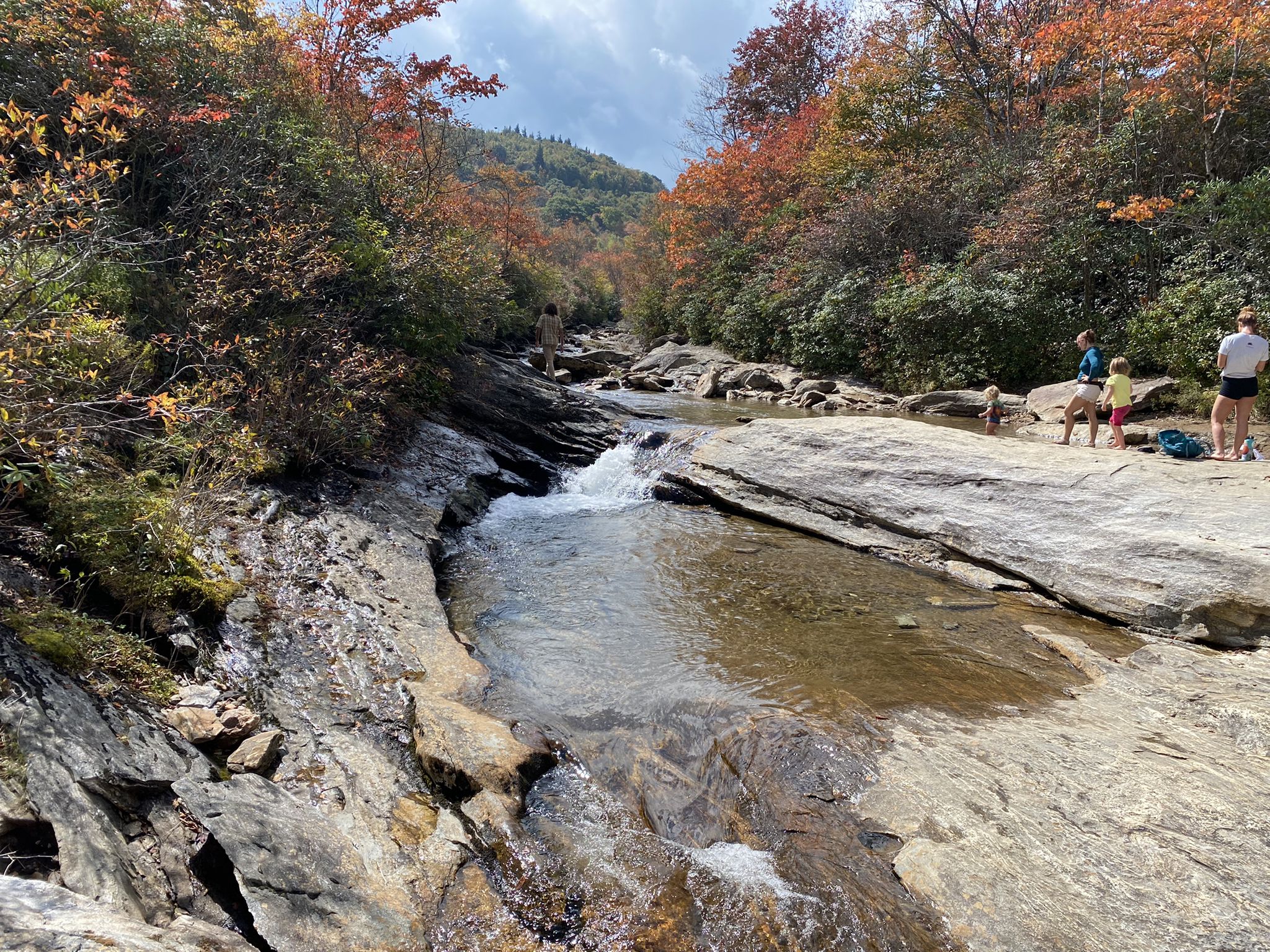 River flowing over rocks, people relaxing on the bank, autumn trees. - Graveyard Ridge Trail and Mountains to Sea Trail Loop