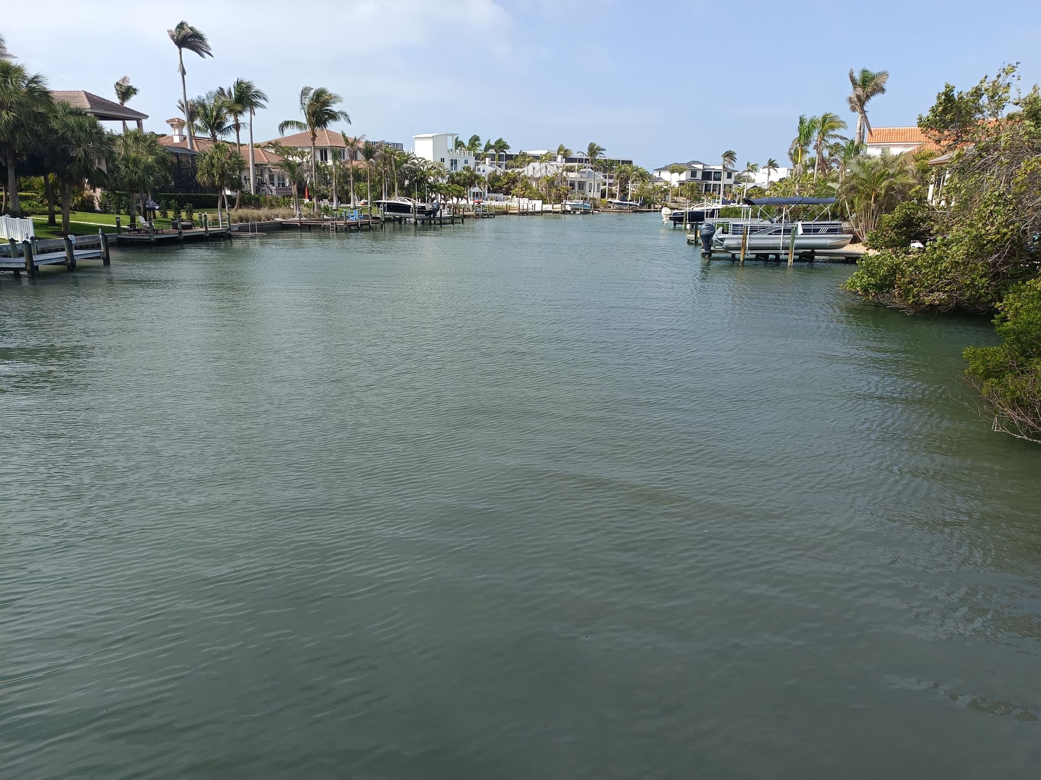 A wide canal with houses, palm trees, and docked boats under bright daylight. - Lido Key loop