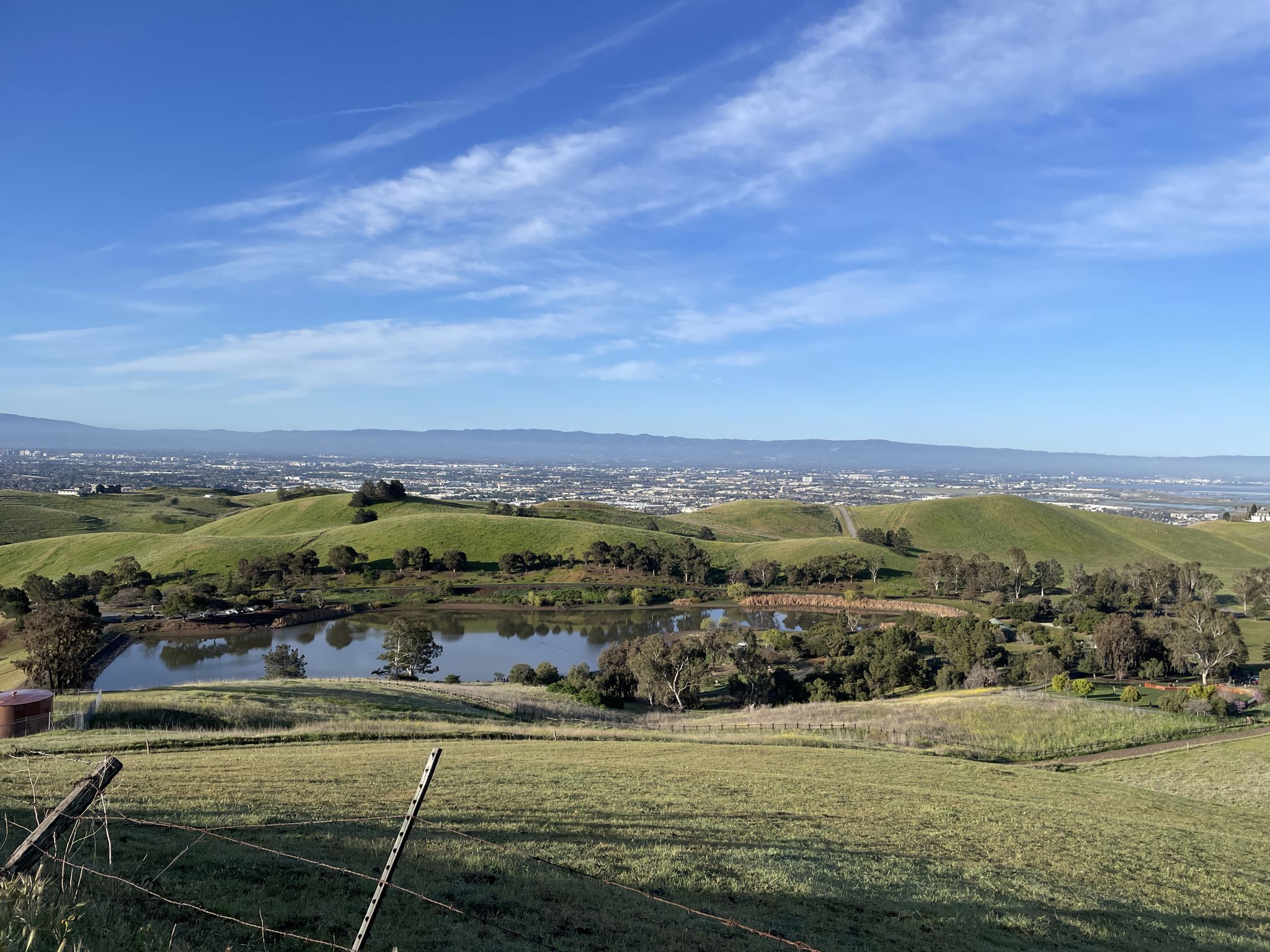 Expansive view of green hills, a calm lake, and a distant city. - Agua Caliente Trail