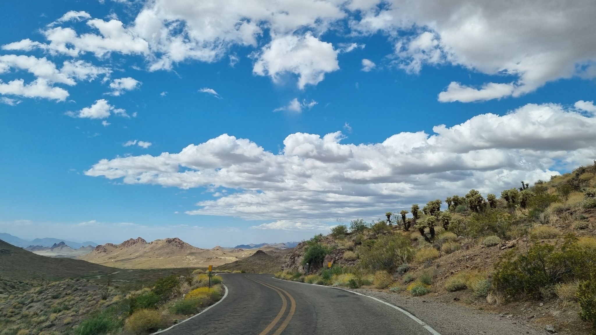 Curved desert road with sparse vegetation under a cloudy blue sky. - Oatman to Sitgreaves Pass via Historic Route 66
