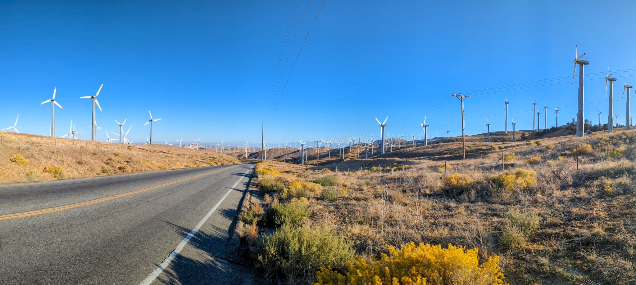 Panoramic view of a road beside numerous wind turbines on arid hills. - Tehachapi Pass loop