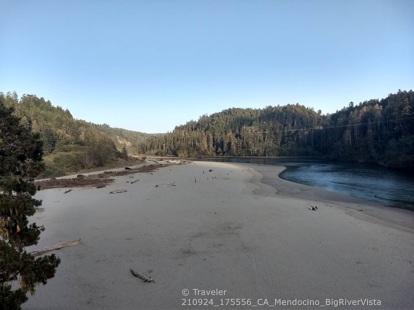 Wide river with sandy banks, surrounded by forested hills under clear sky. - Mendocino - Comptche loop