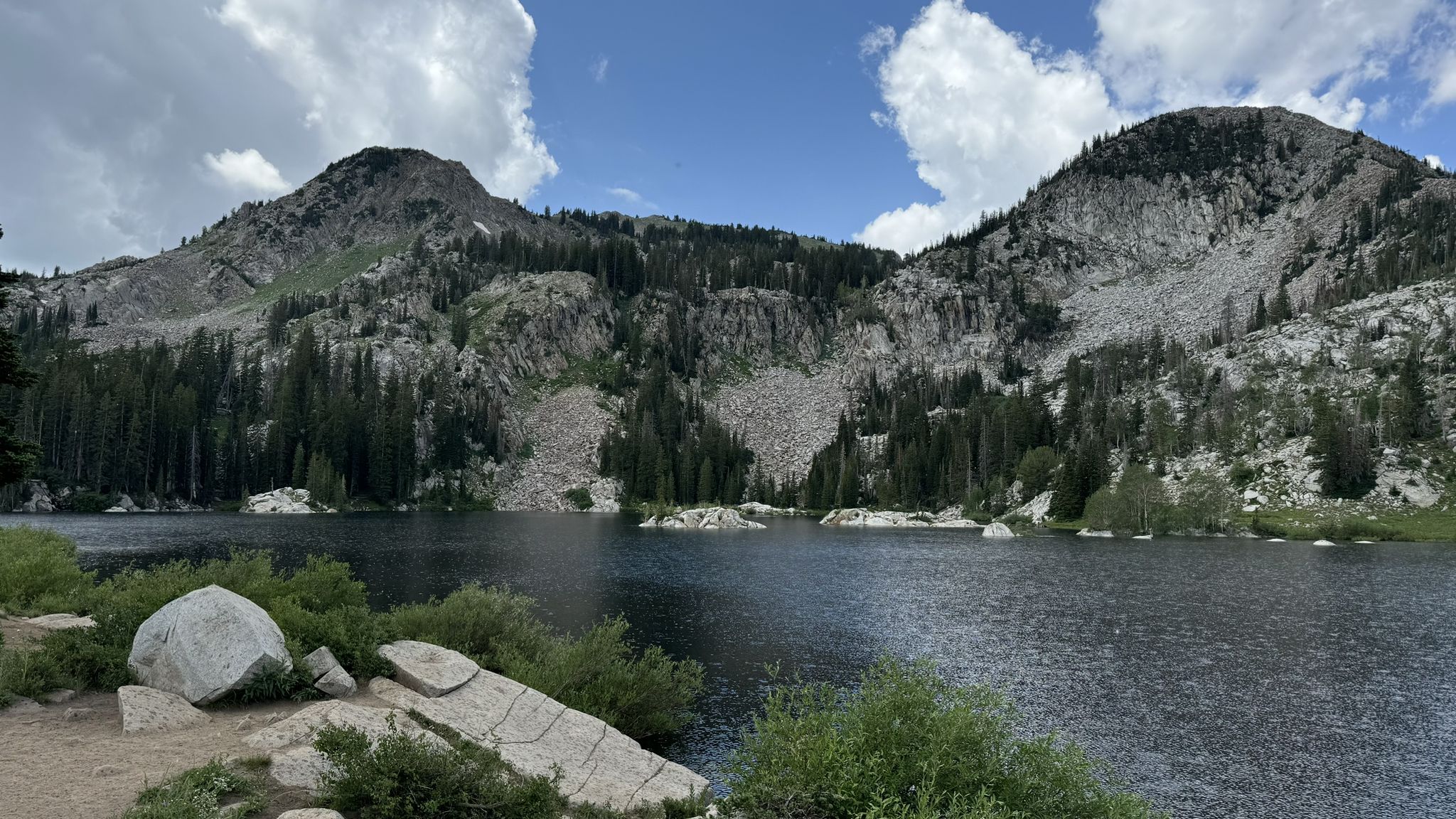 A mountain lake with rocky shores, flanked by two large, forested mountains. - Lake Mary Trail
