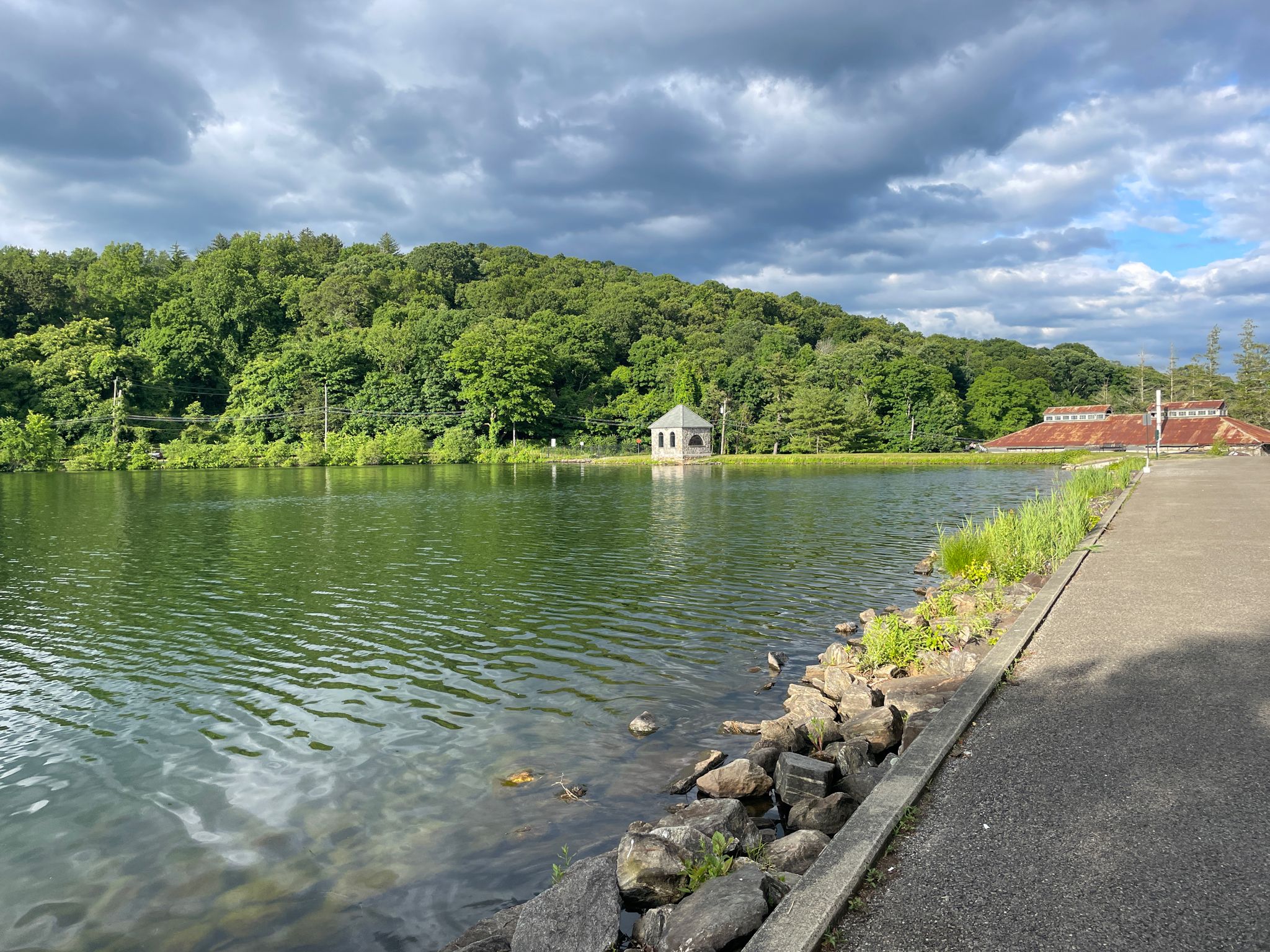 Calm lake with a distant gazebo and lush green forested hills under cloudy sky. - New Croton Reservoir Loop