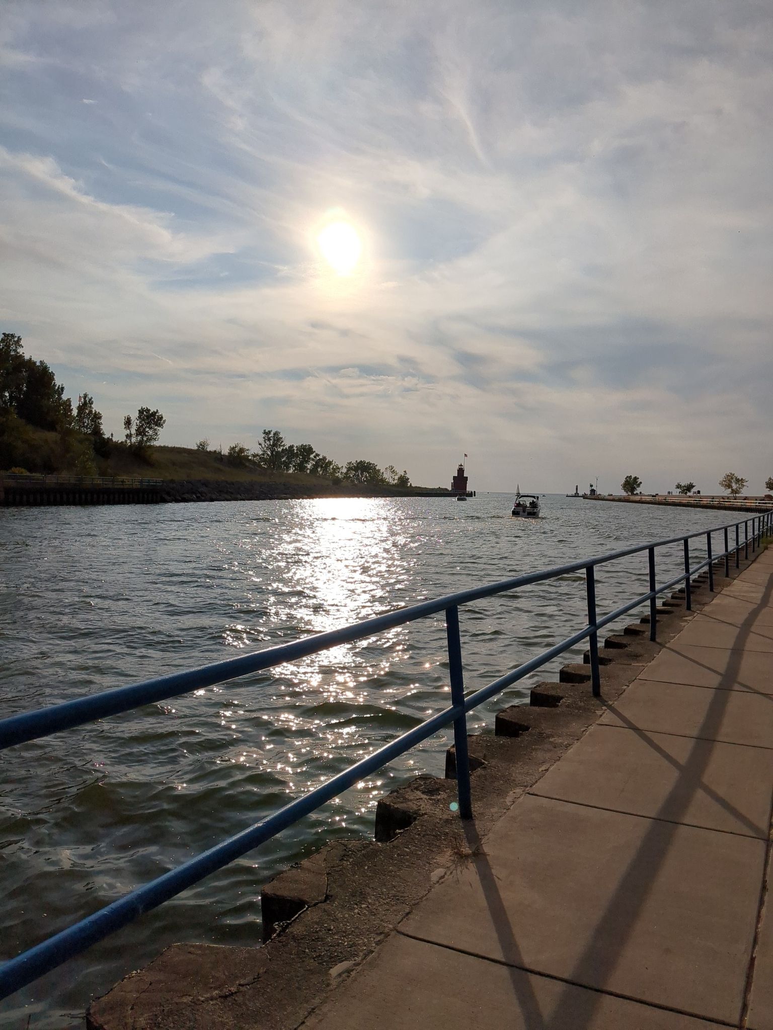 Sunny water reflecting light, concrete pier with blue railing, distant boats. - Lakeshore Trail and Geneva Pines